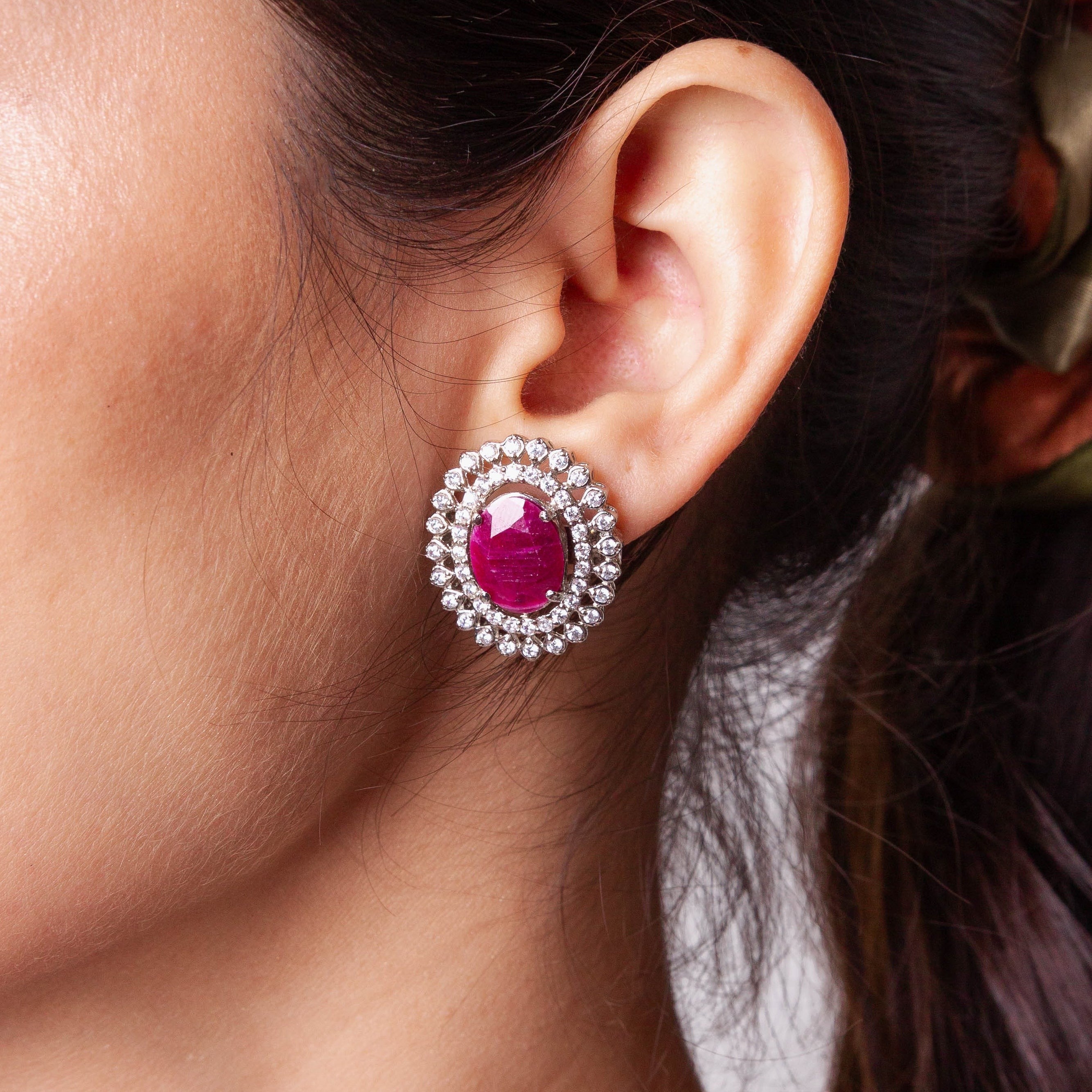 Niz & Aly oval African ruby stud earring surrounded by a sparkling halo of white diamonds on a model's ear.