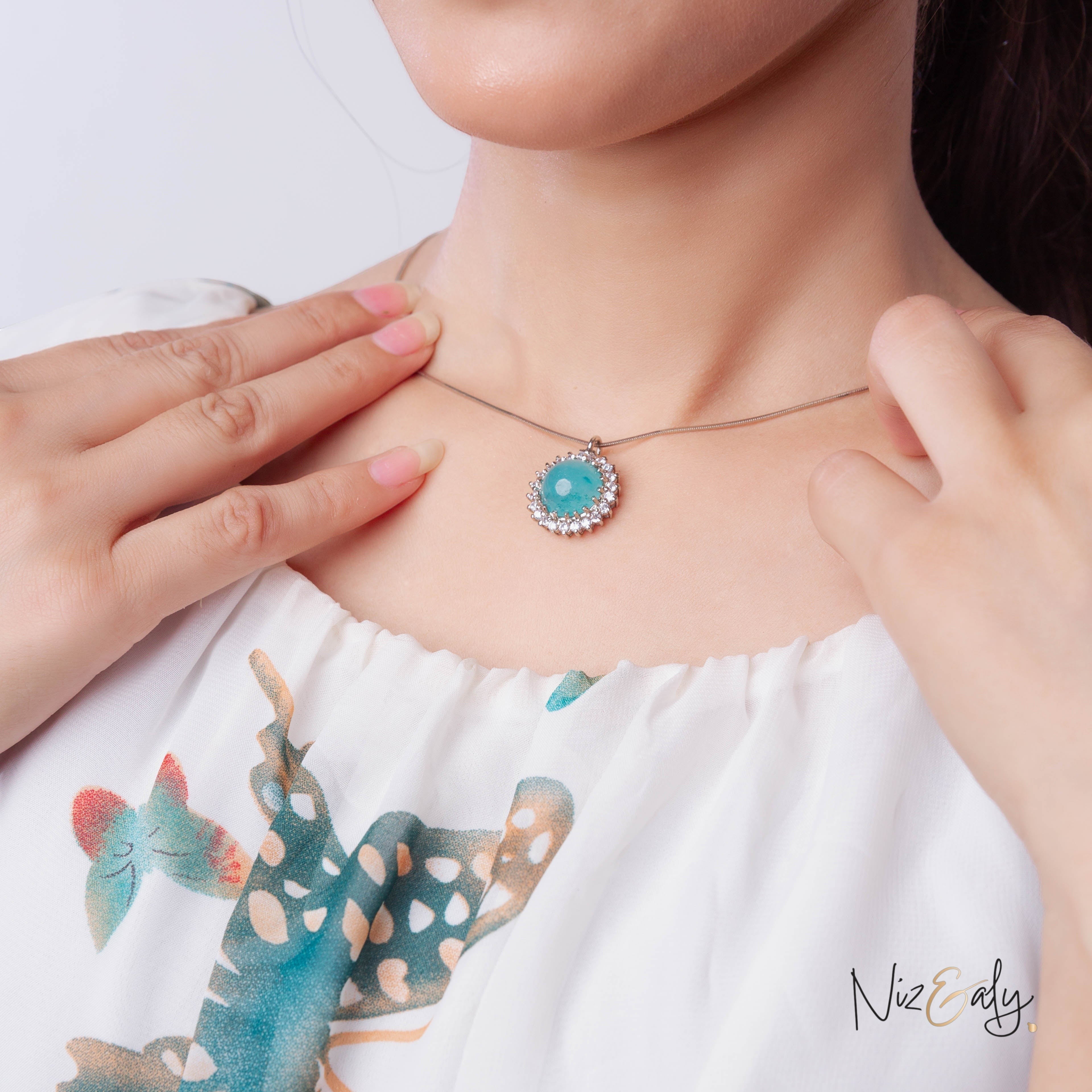 Niz & Aly amazonite pendant necklace with a polished blue-green gemstone surrounded by sparkling crystals on a woman