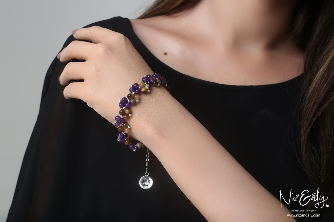 Niz & Aly amethyst and brown banded agate beaded bracelet worn on a woman's wrist with a silver charm.