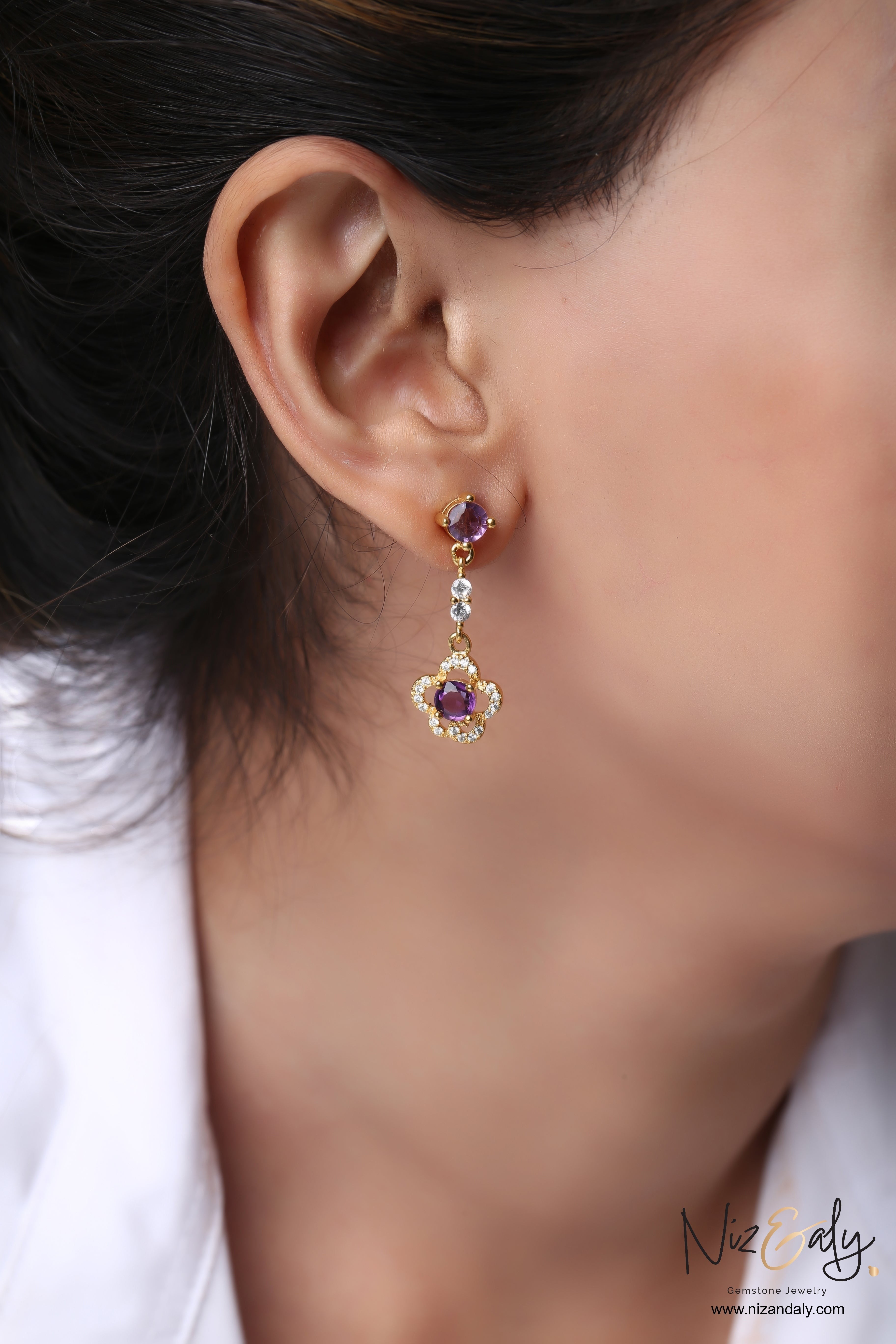Niz & Aly gold plated drop earrings featuring faceted purple amethyst stones and clear crystal accents on a model
