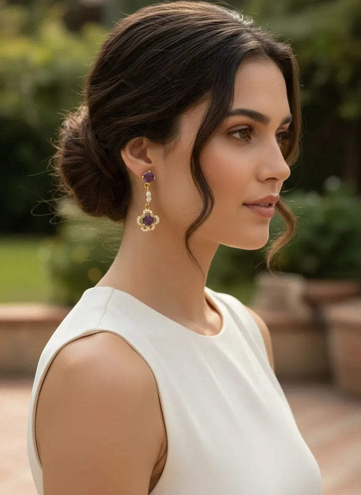 Niz & Aly delicate gold-plated ear drops featuring faceted purple amethyst gemstones worn by a woman in a white dress.