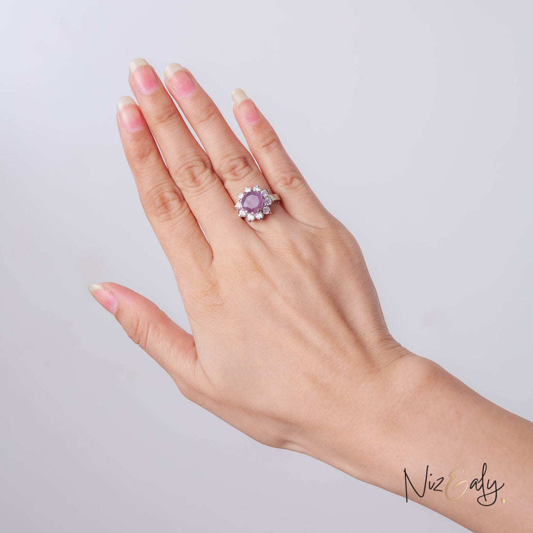 Niz & Aly amethyst and diamond halo ring worn on a woman's finger, featuring a deep violet gemstone in silver setting.