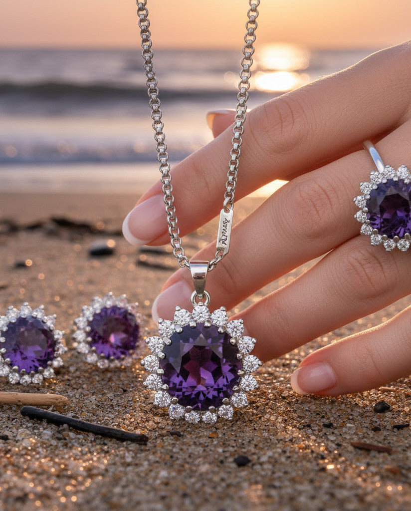 Niz & Aly Amethyst Serenity Locket Set featuring a purple gemstone pendant, matching earrings, and ring on a beach.