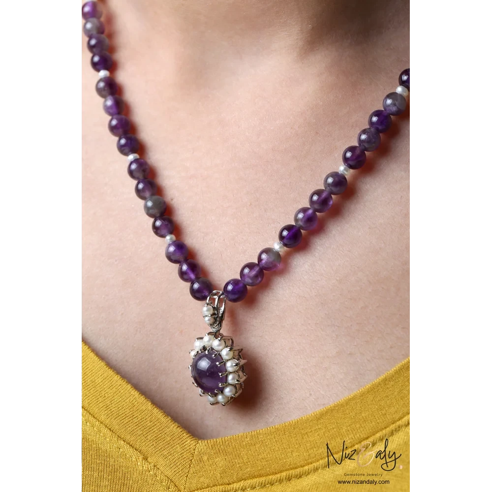 Niz & Aly amethyst and pearl pendant necklace with purple beaded strand worn on a person in a yellow top