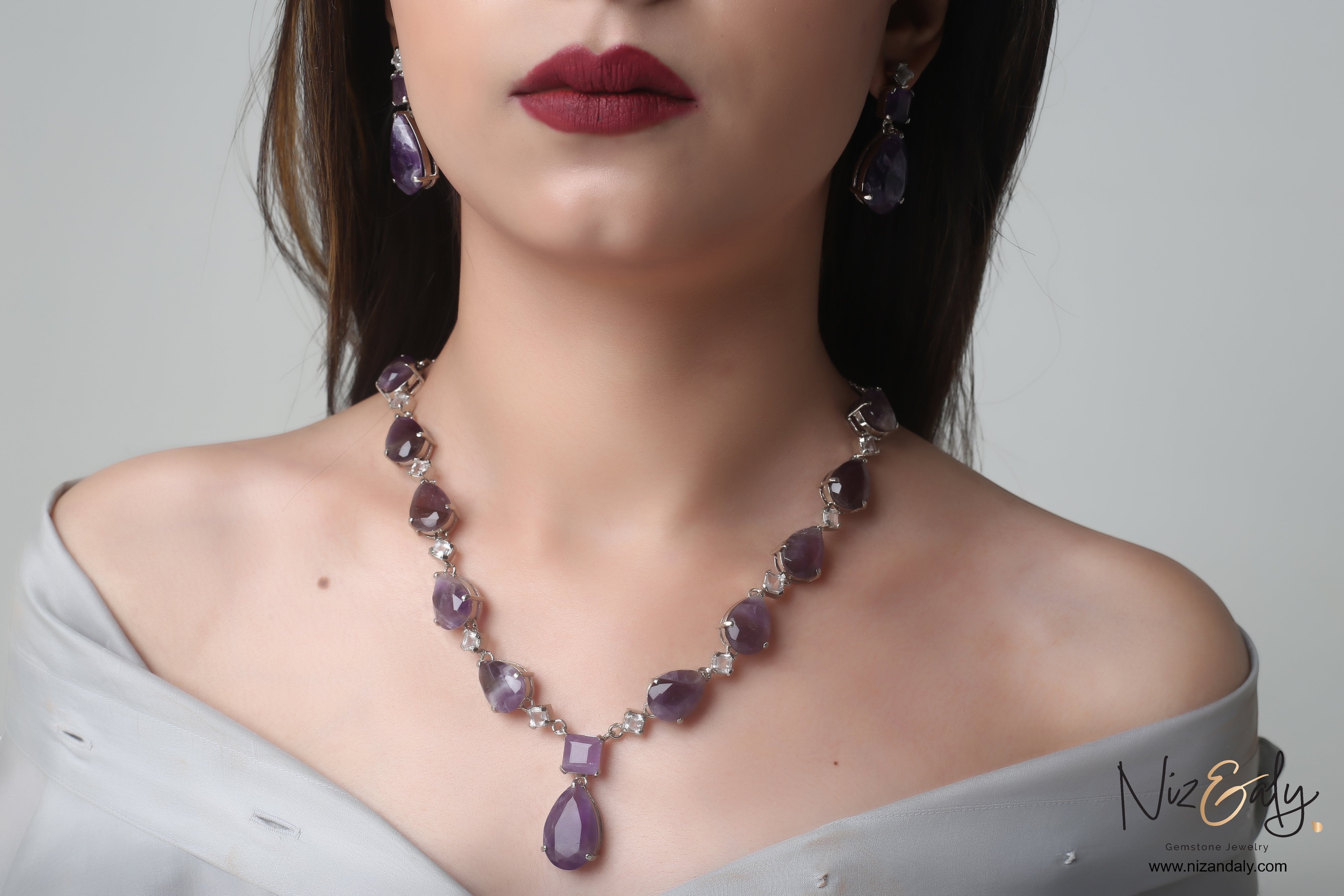 Niz & Aly necklace set with droplet-cut amethyst and clear quartz gemstones worn by a model in a grey off-shoulder top