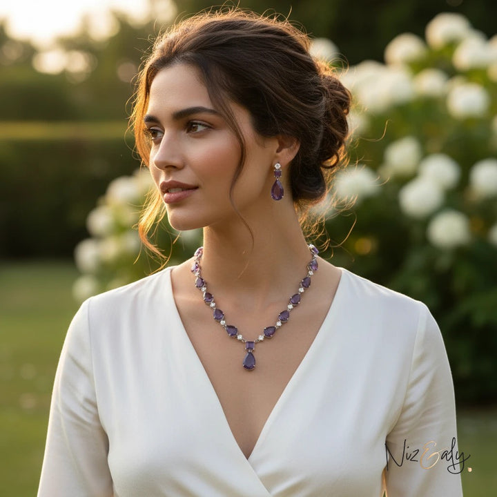 Niz & Aly necklace set featuring droplet amethyst and clear quartz worn by a woman in a white dress outdoors.