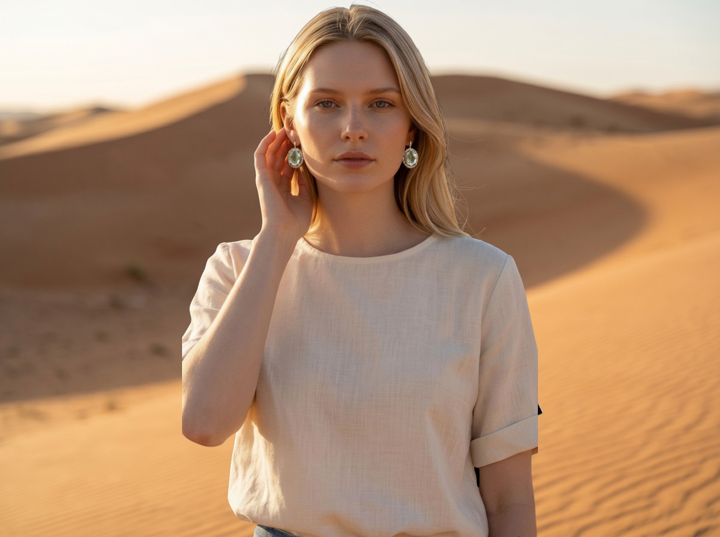 Niz & Aly oval aquamarine halo stud earrings worn by a woman in a desert setting at sunset.
