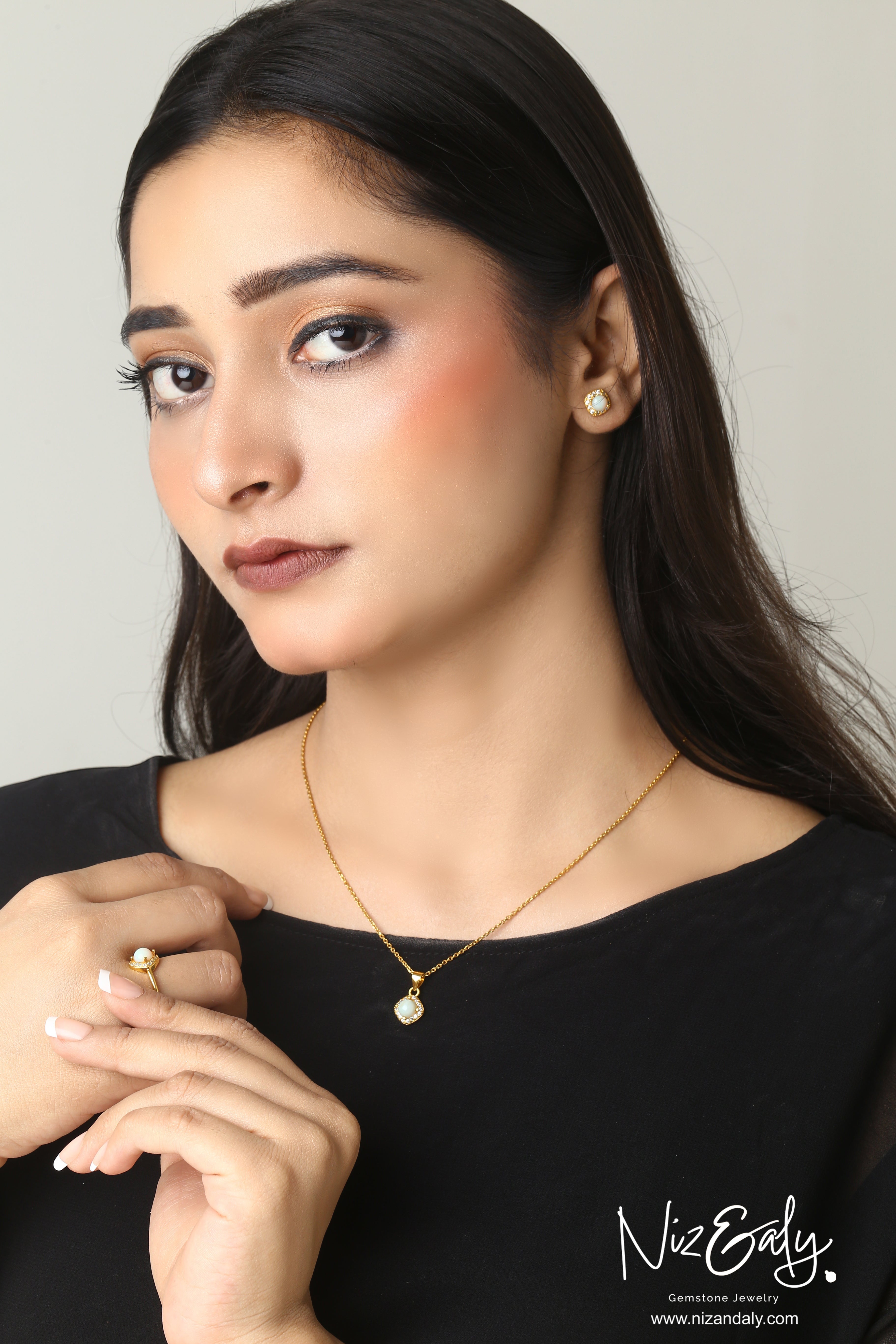 Model wearing Niz & Aly gold-plated Australian opal necklace, stud earrings, and ring with geometric halo settings.