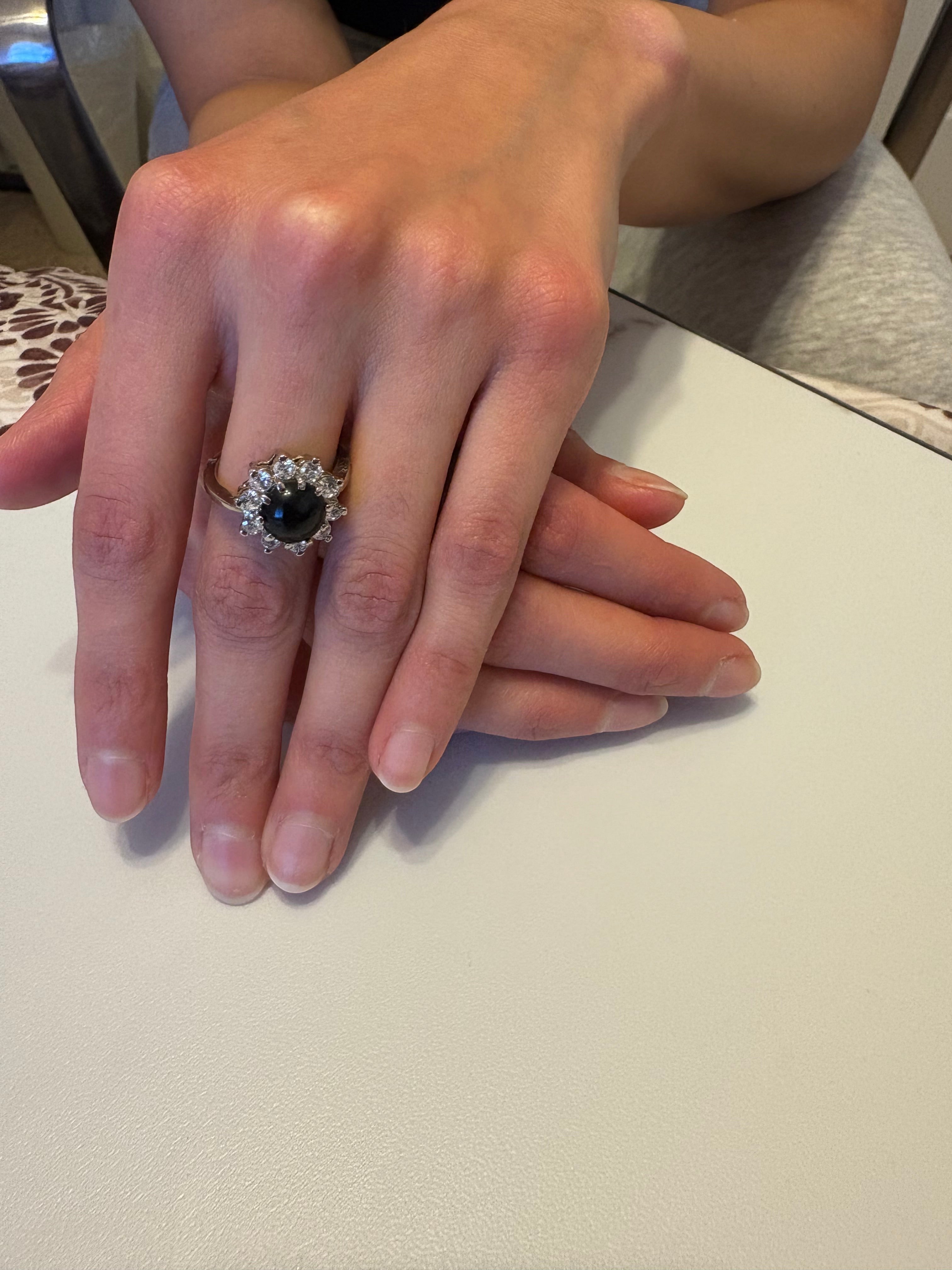 Niz & Aly natural black onyx ring with a halo of sparkling stones on an adjustable silver band worn on a hand.