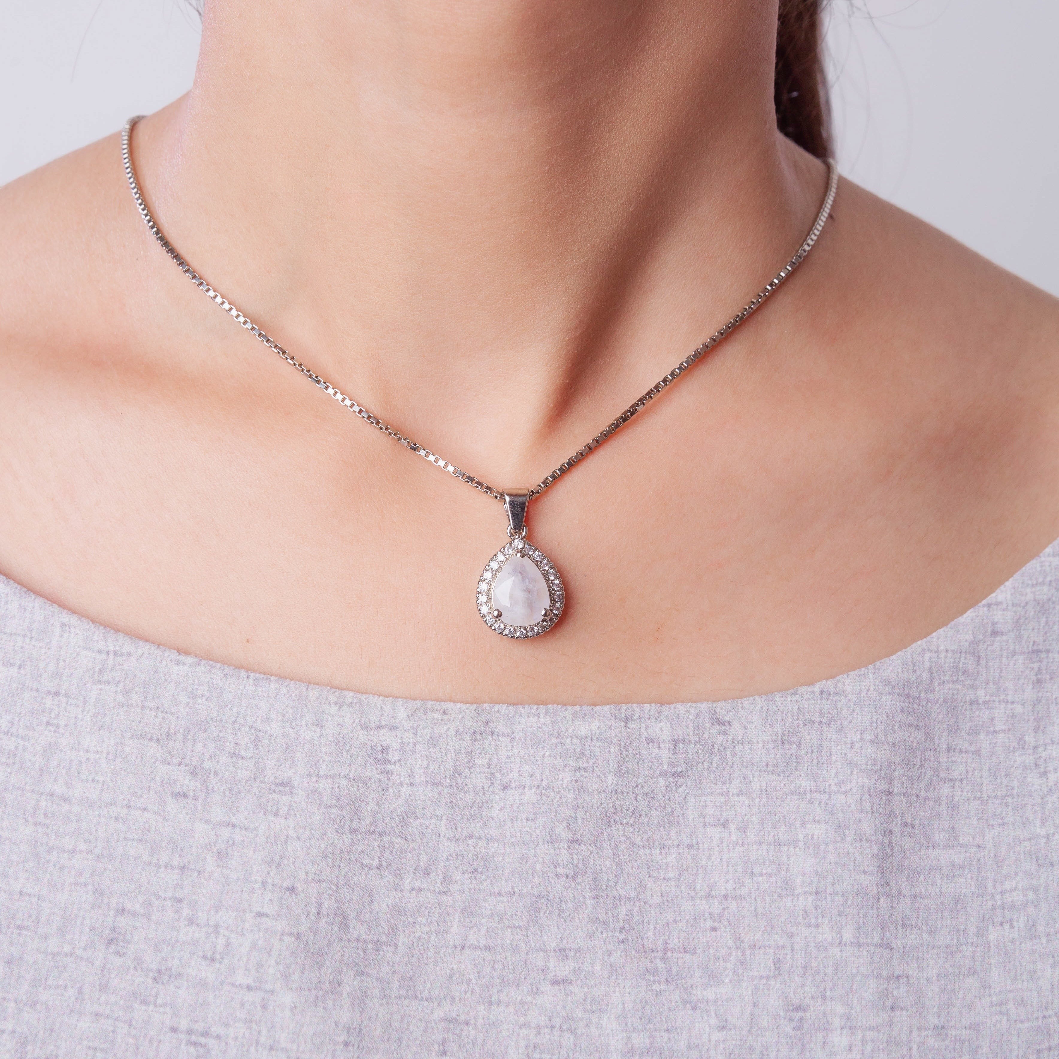 Niz & Aly blue flash moonstone pendant necklace with a halo of sparkling stones on a silver chain worn on a neck