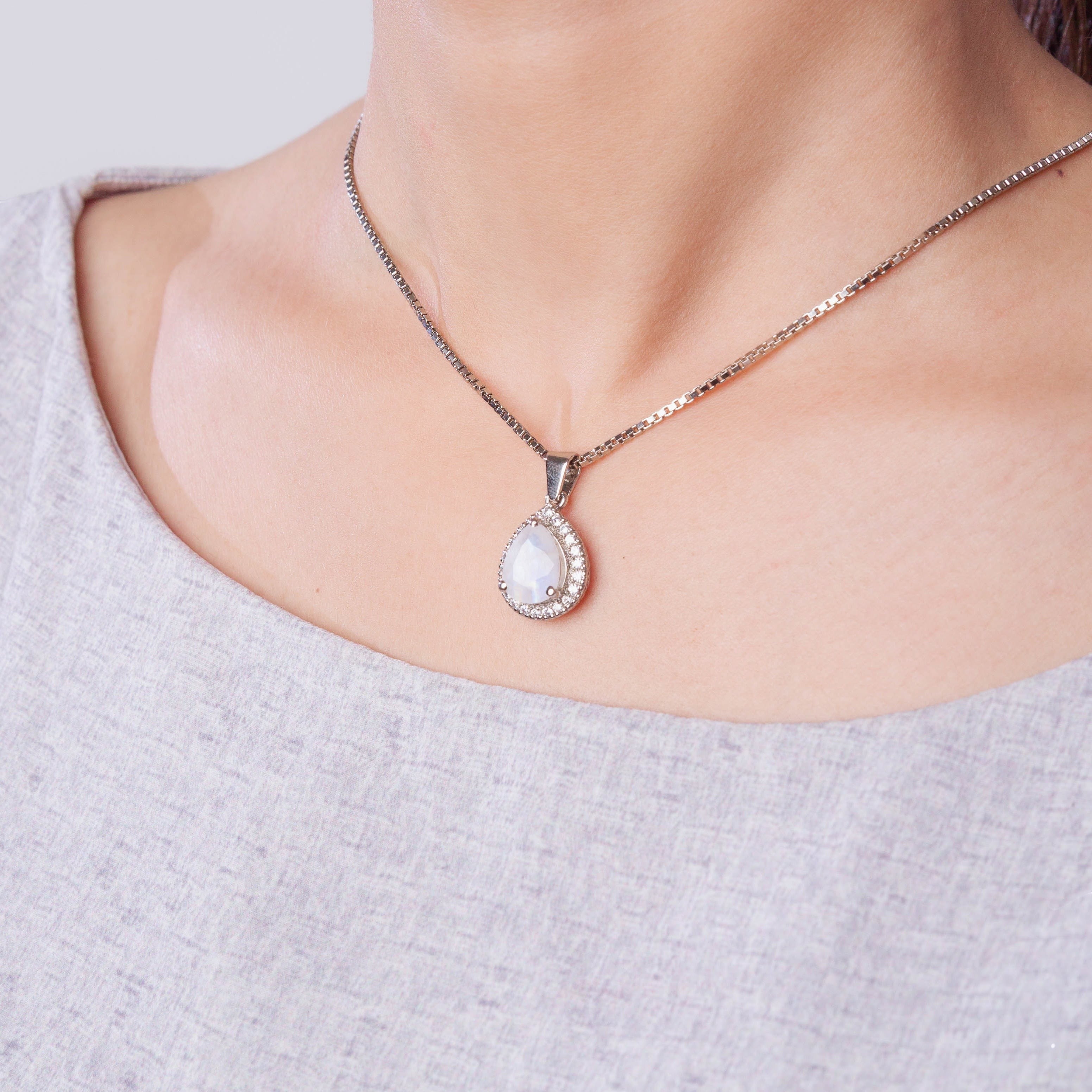 Niz & Aly blue flash moonstone pendant in a teardrop shape with a silver chain worn around a woman's neck