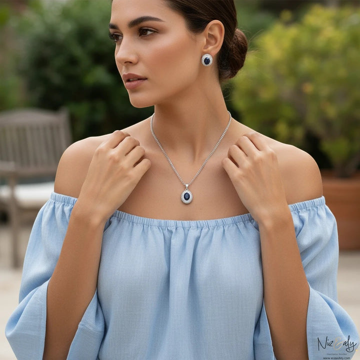 Niz & Aly royal blue natural sapphire pendant and matching stud earrings worn by a woman in a light blue top