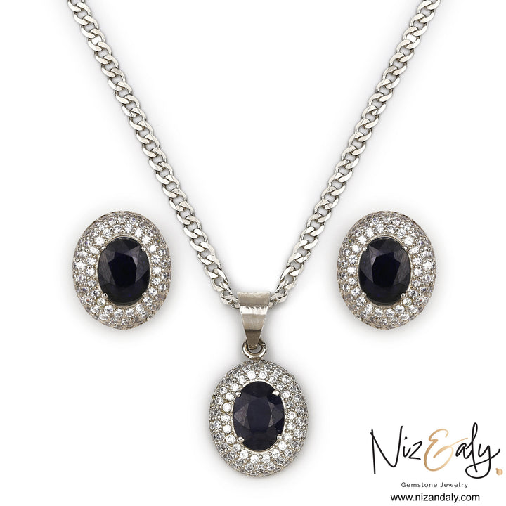 Niz & Aly royal blue sapphire pendant and stud earring set with diamond halo accents on a silver chain.