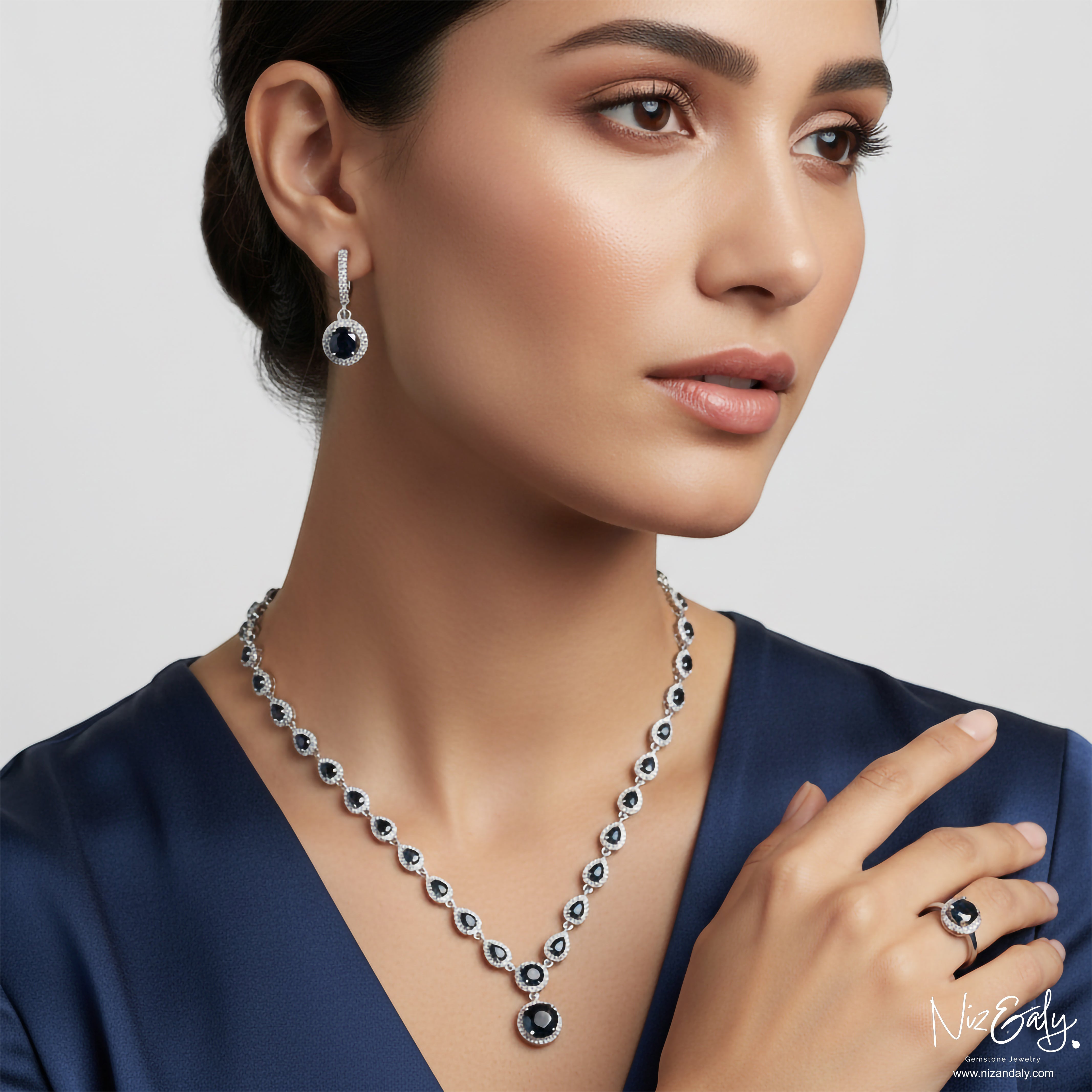 Niz & Aly blue sapphire and sterling silver necklace, earring, and ring set worn by a woman in a navy dress.