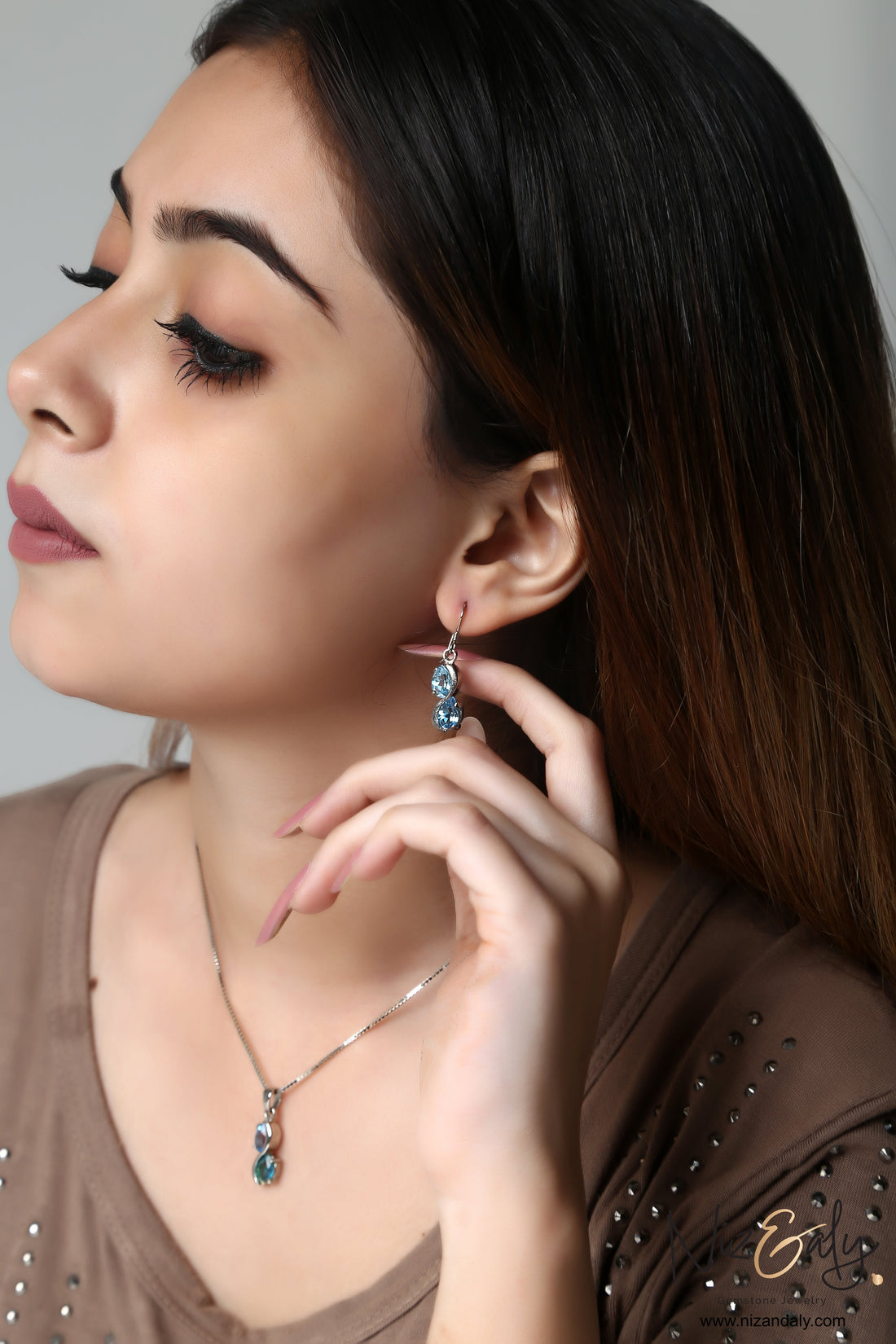 Niz & Aly sea blue double topaz drop pendant and earring set worn by a woman with a soft brown top.