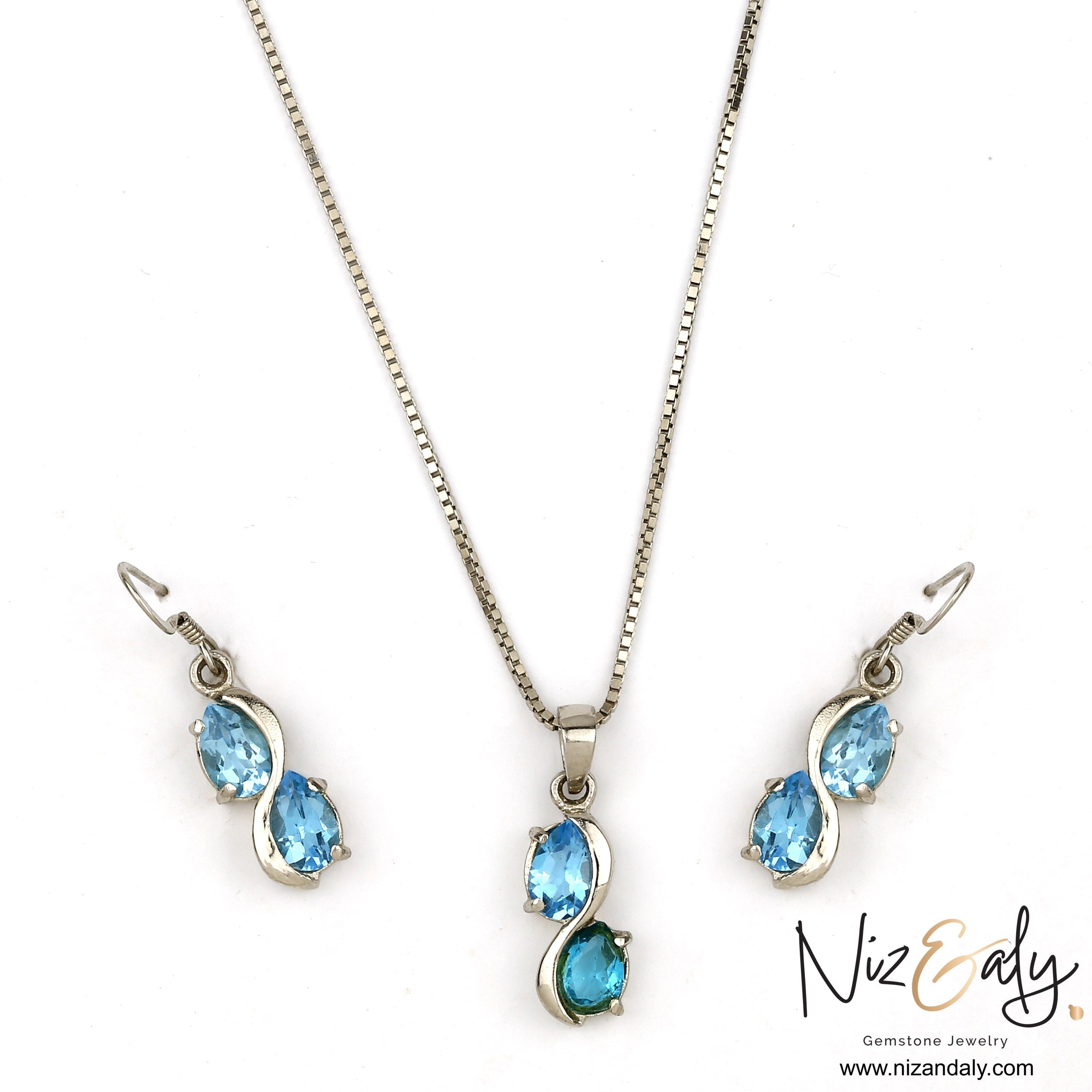 Niz & Aly sea blue double topaz drop pendant and earring set in silver, featuring shimmering oval gemstones.
