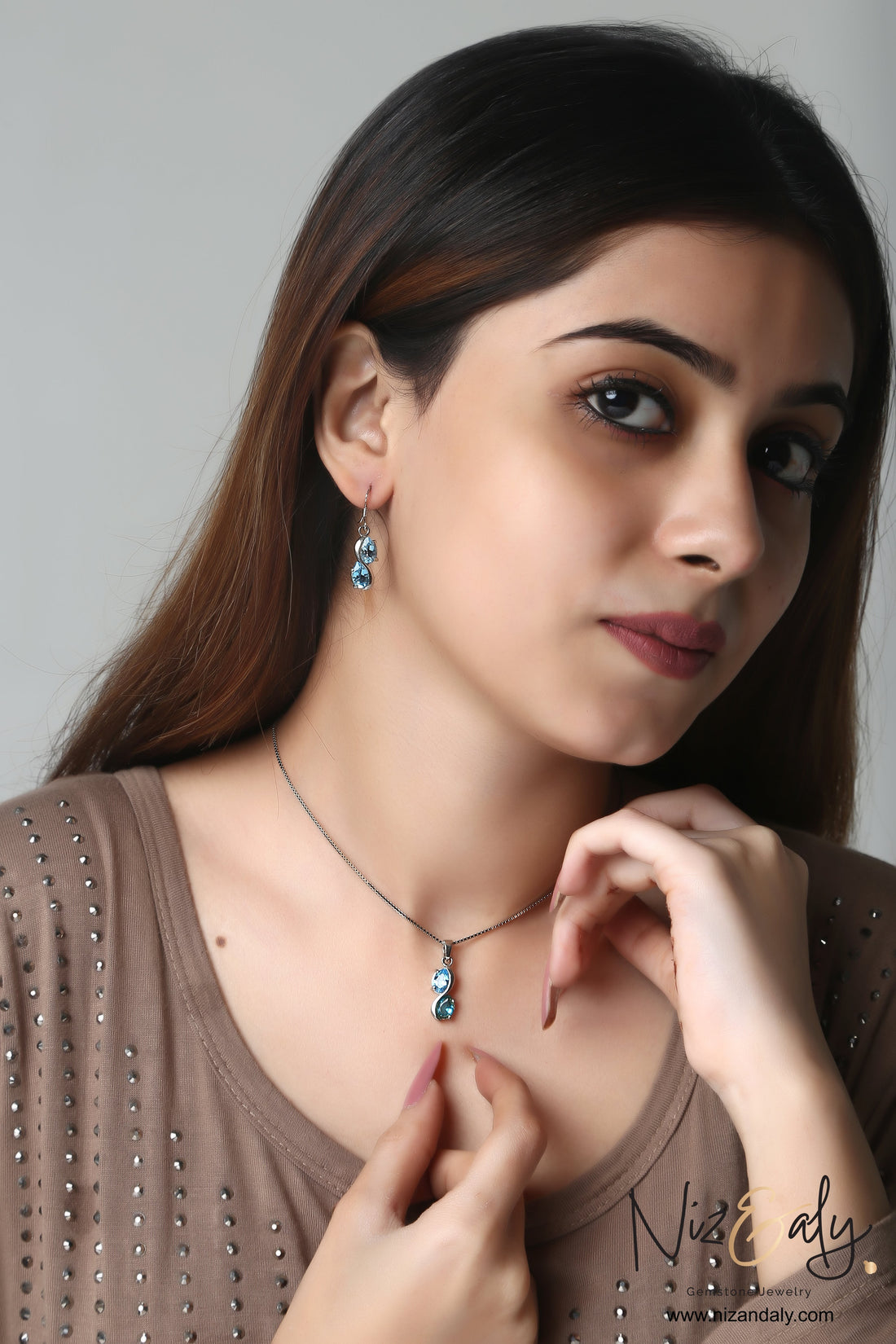 Niz & Aly sea blue double topaz pendant and earring set worn by a woman, featuring luminous teardrop gemstones.