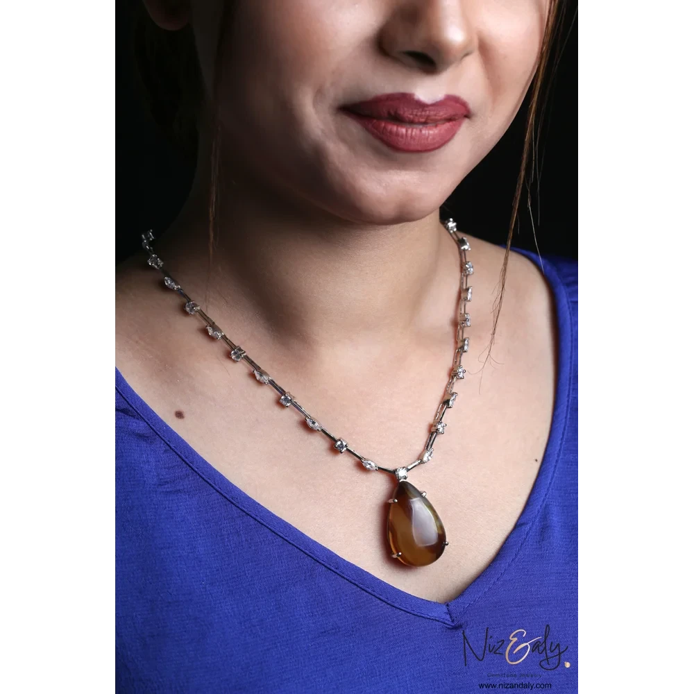 Niz & Aly brown agate teardrop pendant necklace with cubic zirconia accents worn on a model in a blue top.
