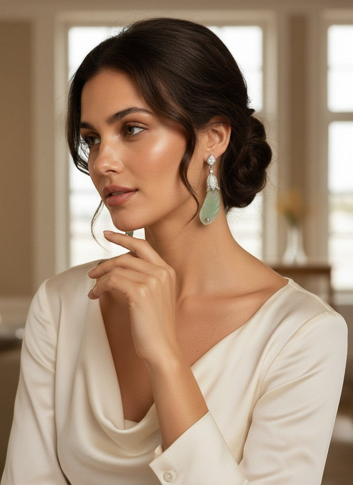 Niz & Aly carved prehnite ear drops with delicate green gemstone pendants worn by a woman in a cream silk blouse.