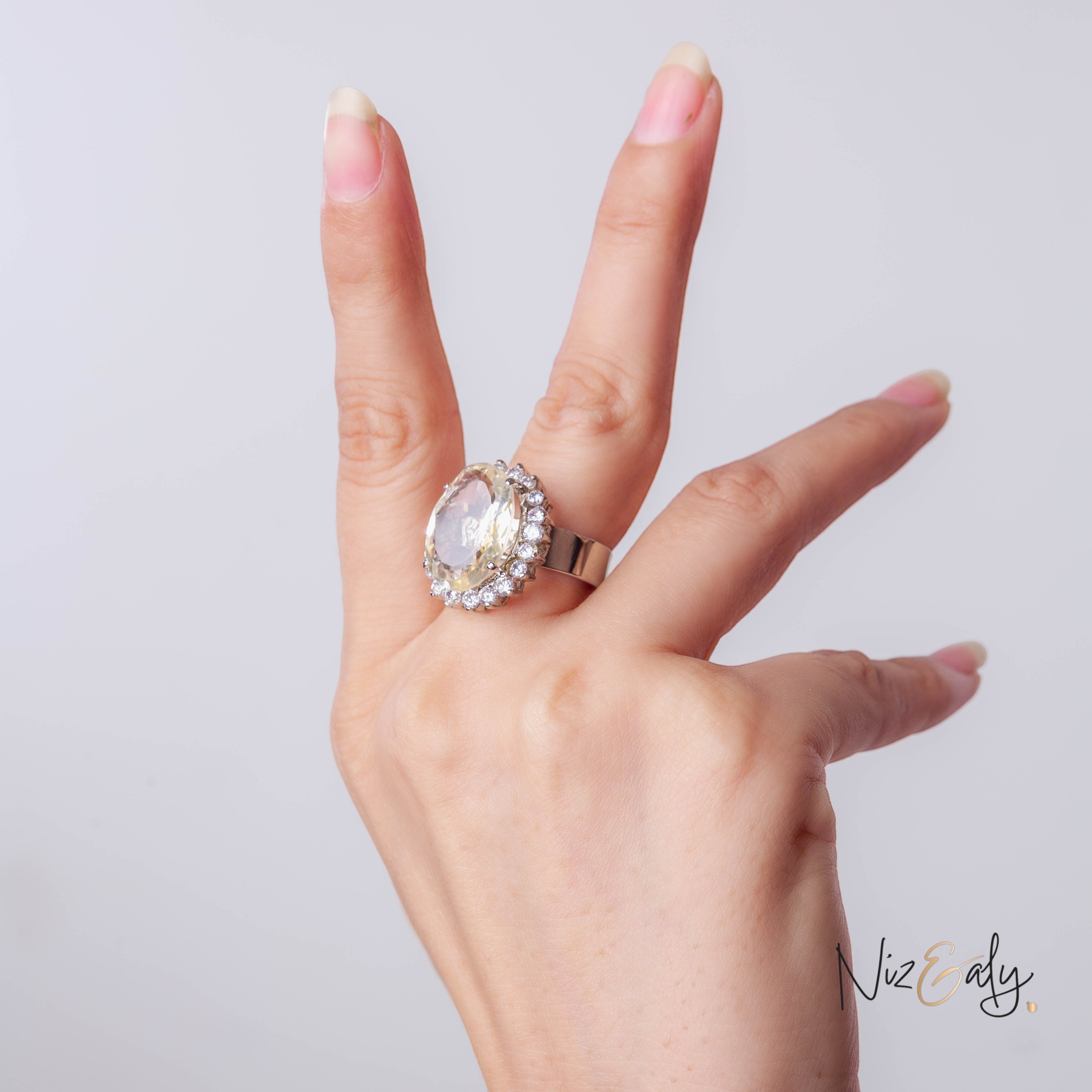 Niz & Aly designer ring featuring a large oval citrine stone surrounded by a halo of small diamonds on a silver band.