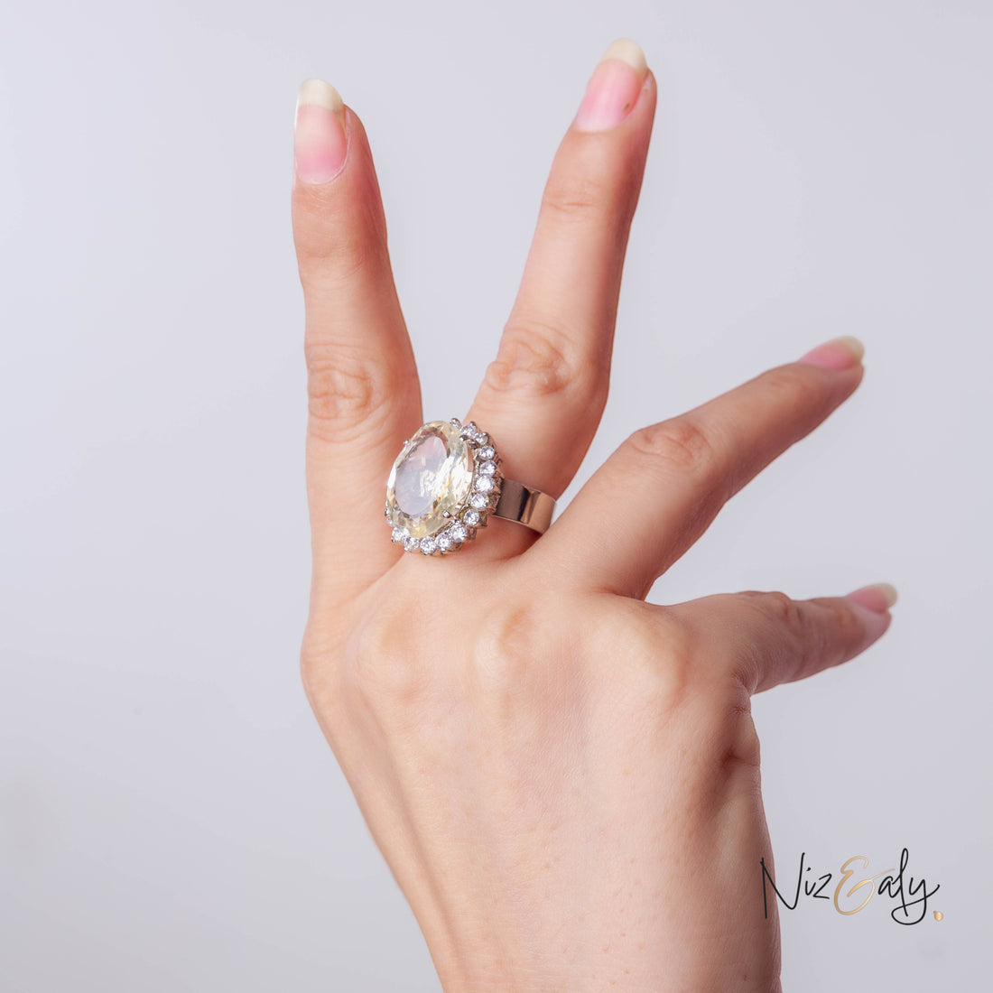 Niz & Aly designer ring featuring a large oval citrine stone surrounded by a halo of small diamonds on a silver band.