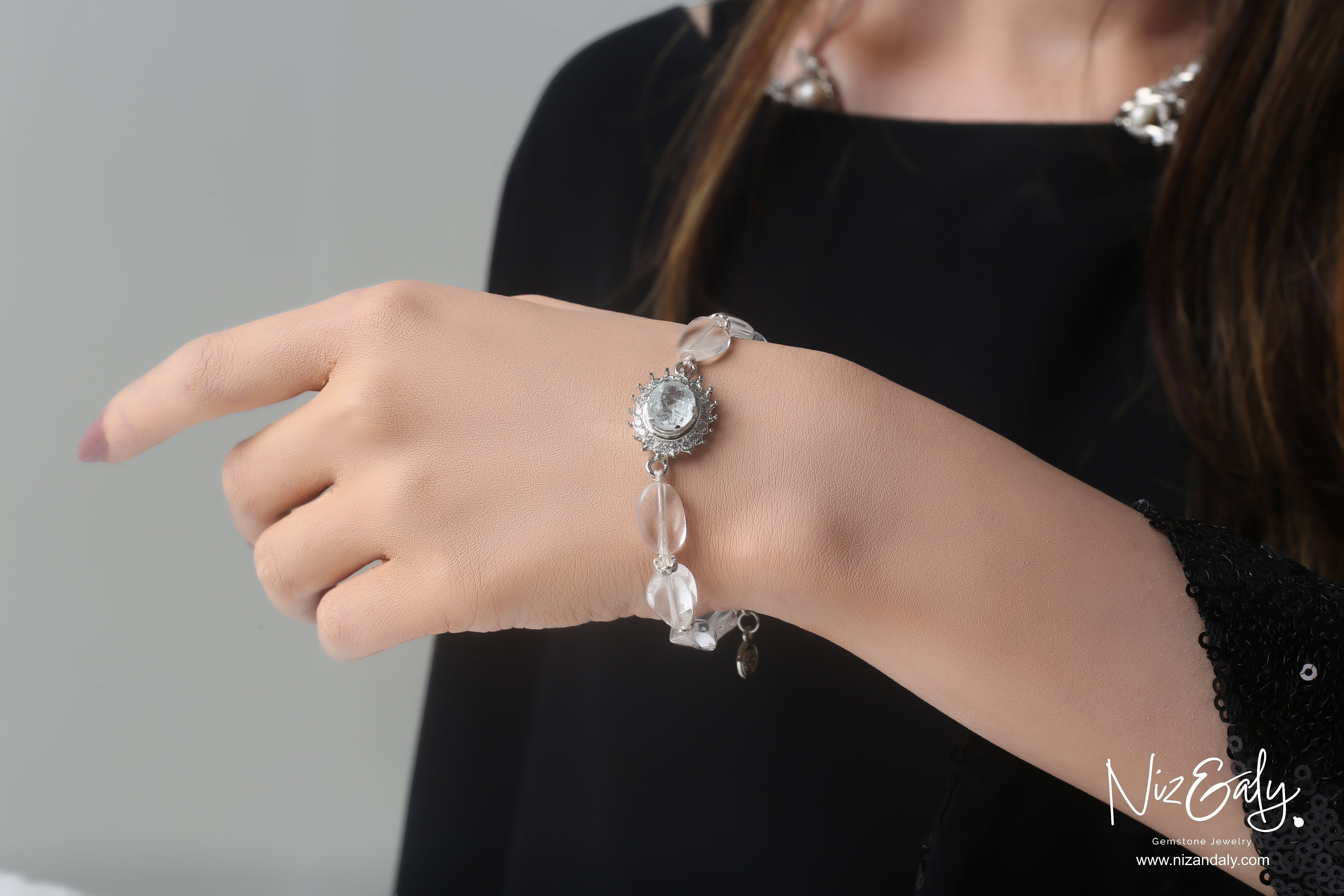 Niz & Aly clear quartz beaded bracelet with a central crystal charm worn on a woman's wrist against a black top.