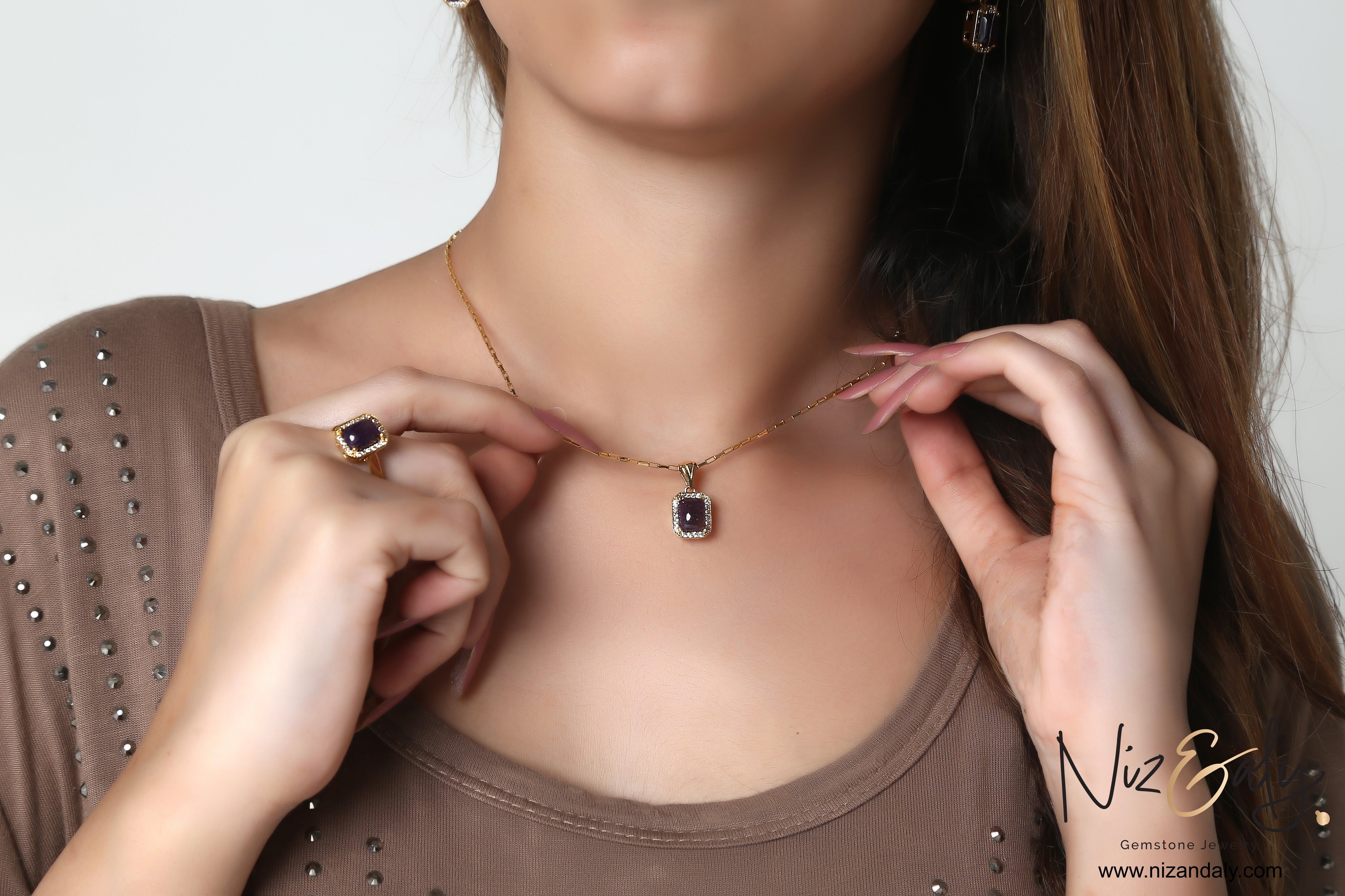 Niz & Aly cushion cut dark amethyst pendant necklace and matching ring worn by a model in a brown top