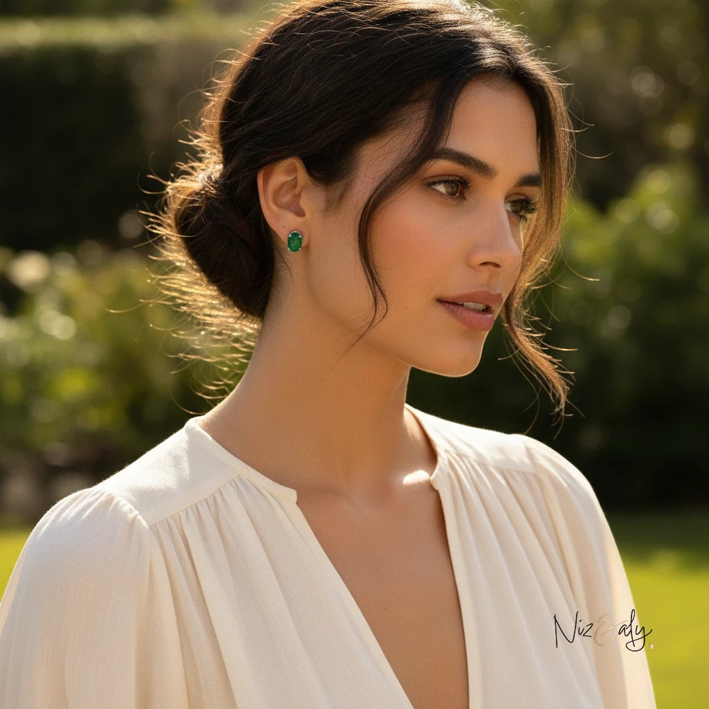 Niz & Aly dainty emerald ear studs worn by a woman in a white blouse, highlighting the vibrant green gemstone.
