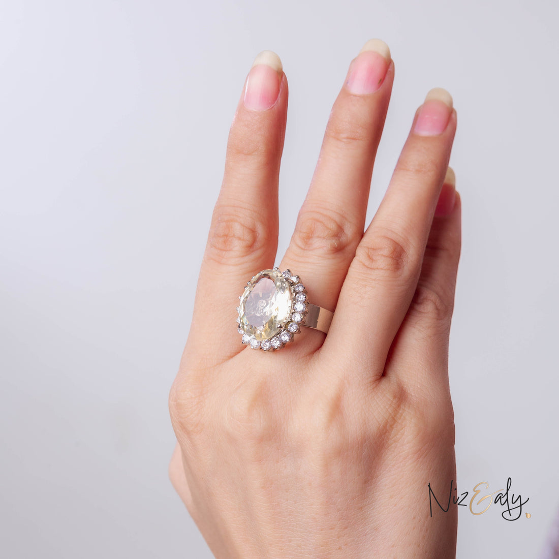 Niz & Aly Designer's Citrine Ring featuring a large oval yellow gemstone surrounded by small diamonds on a silver band