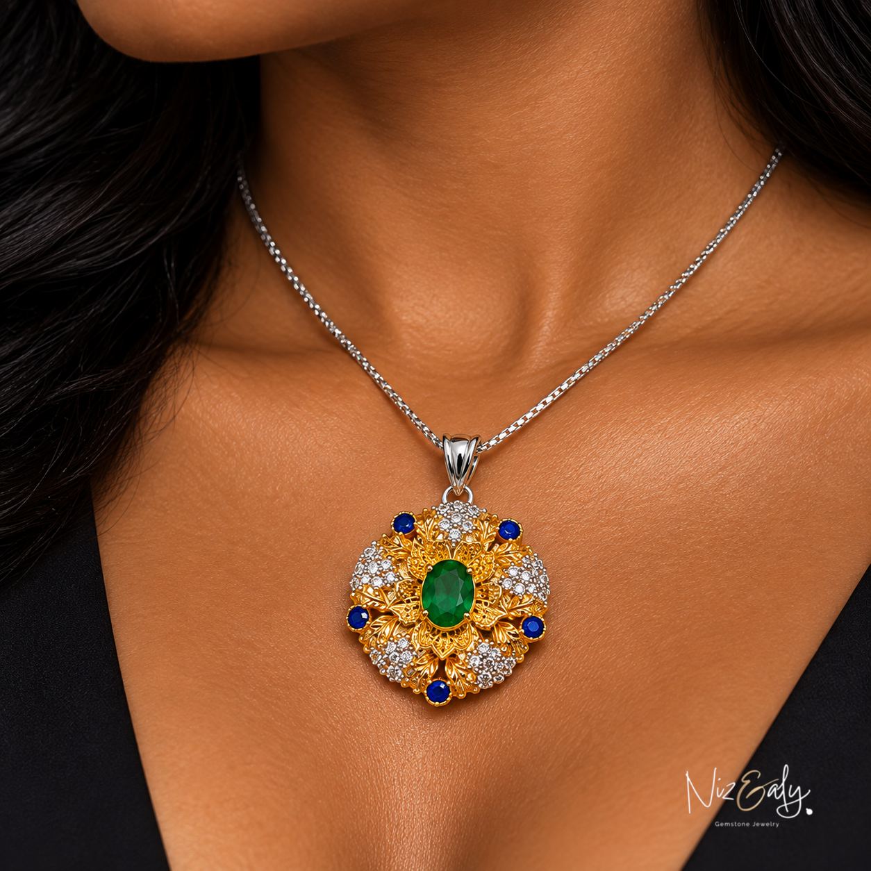 Niz & Aly emerald pendant necklace with gold filigree, diamond accents, and blue sapphire stones on a silver chain.