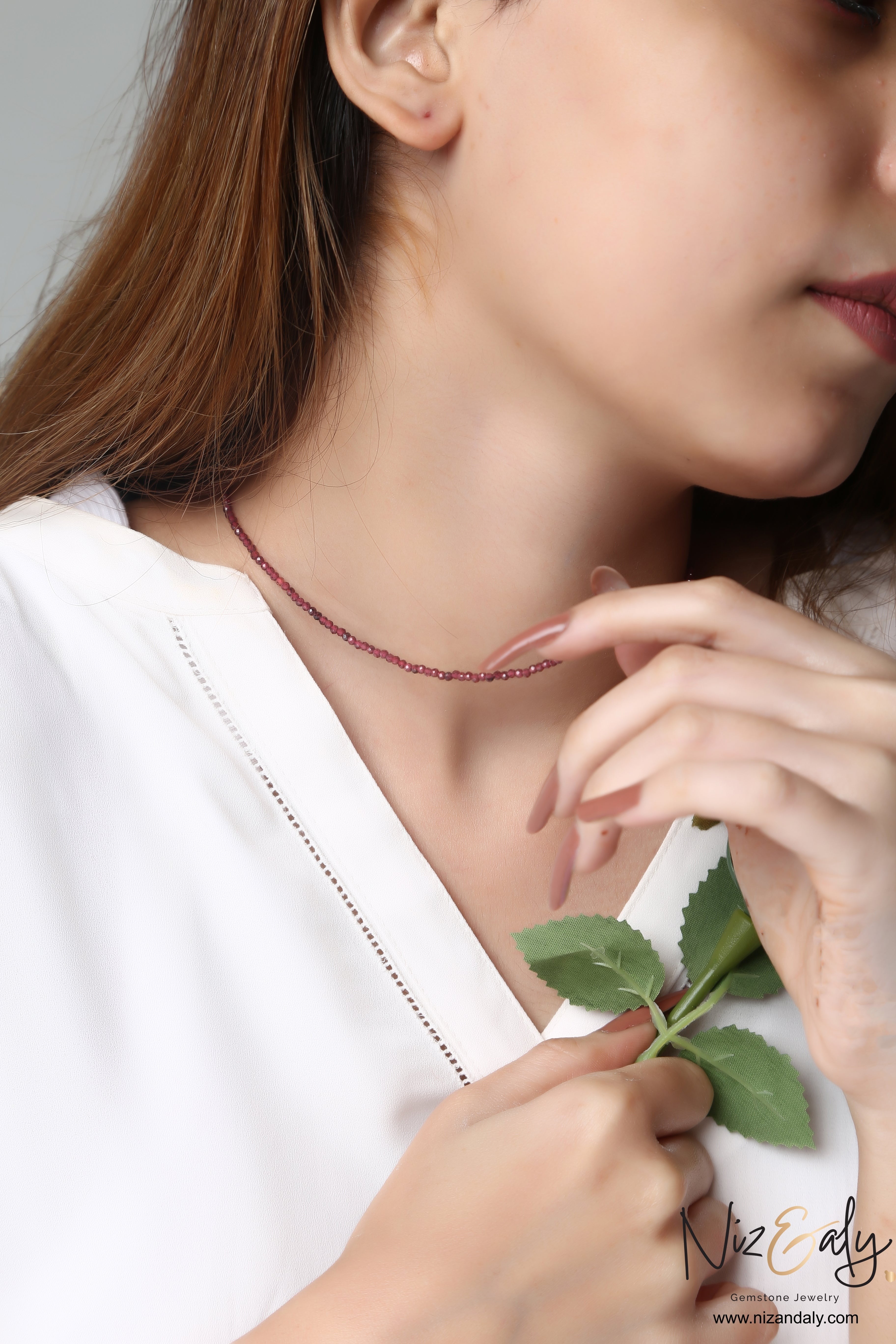 Niz & Aly dainty faceted almandine garnet bead necklace worn on a woman's neck, showcasing deep red gemstone shimmer.