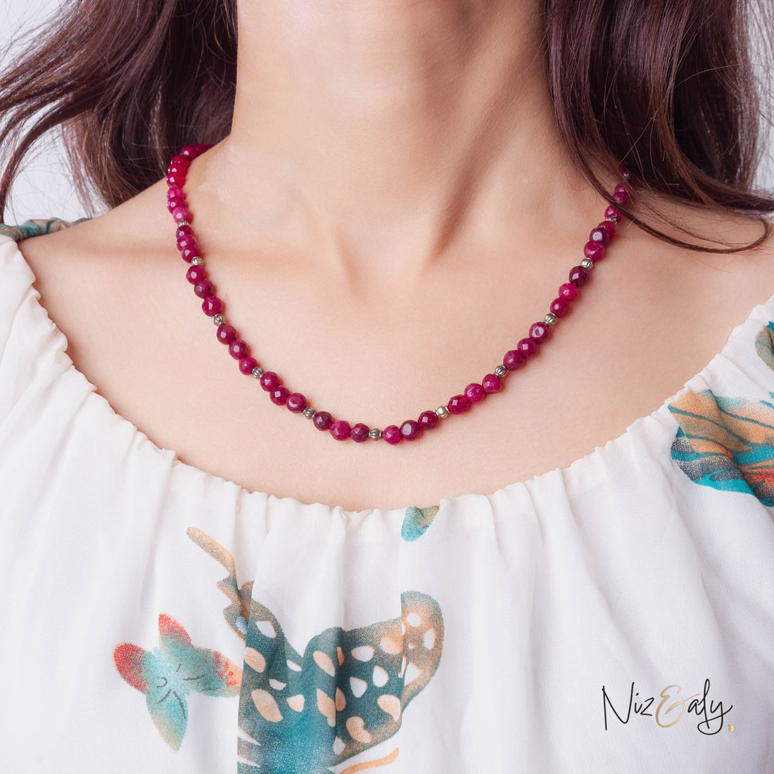 Niz & Aly faceted almandine garnet bead necklace worn by a woman in a white floral top, showing deep red gemstones.