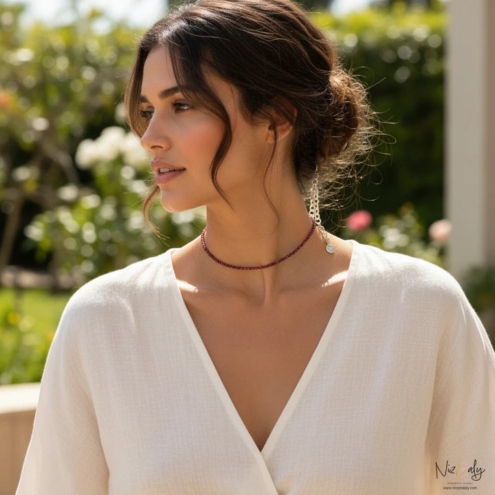 Niz & Aly dainty faceted almandine garnet bead choker necklace worn by a woman in a white top in a garden setting.