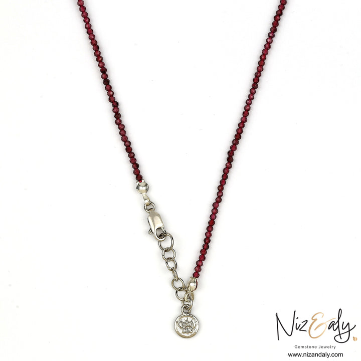 Niz & Aly dainty faceted almandine garnet bead necklace with a silver clasp and charm on a white background.