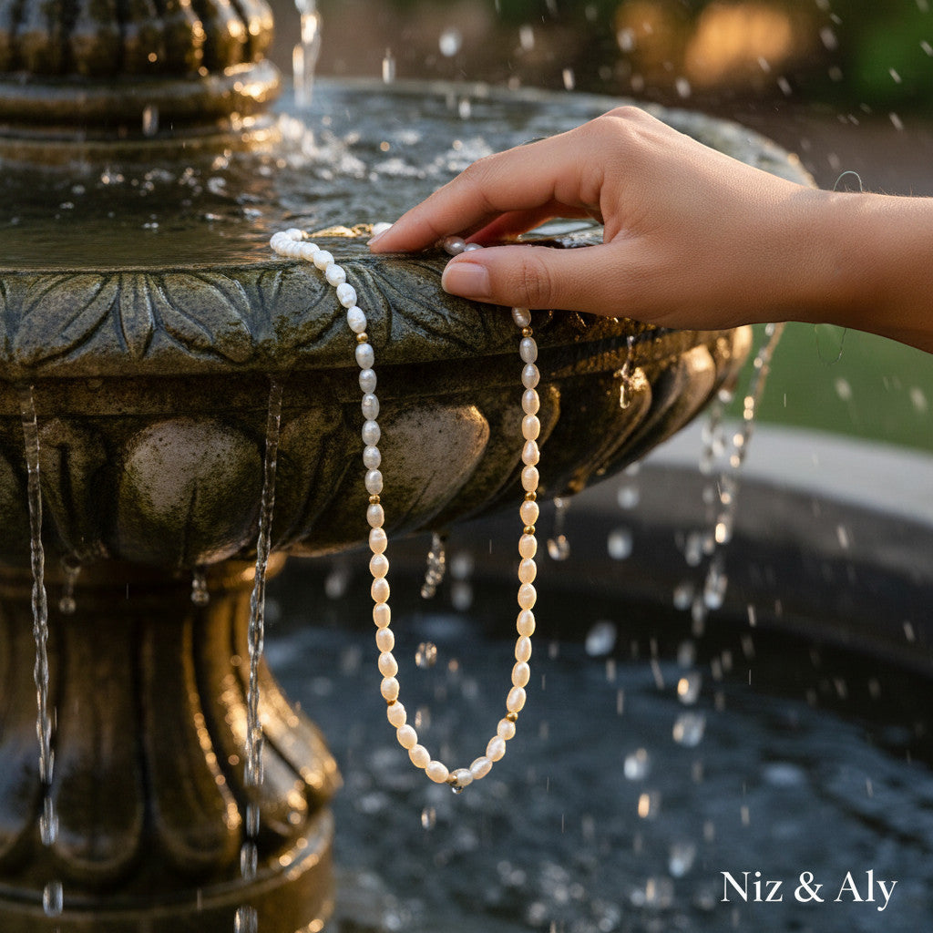 Niz & Aly Pearl Harvest necklace featuring rice-shaped freshwater pearls and 14k gold accents held near a fountain.