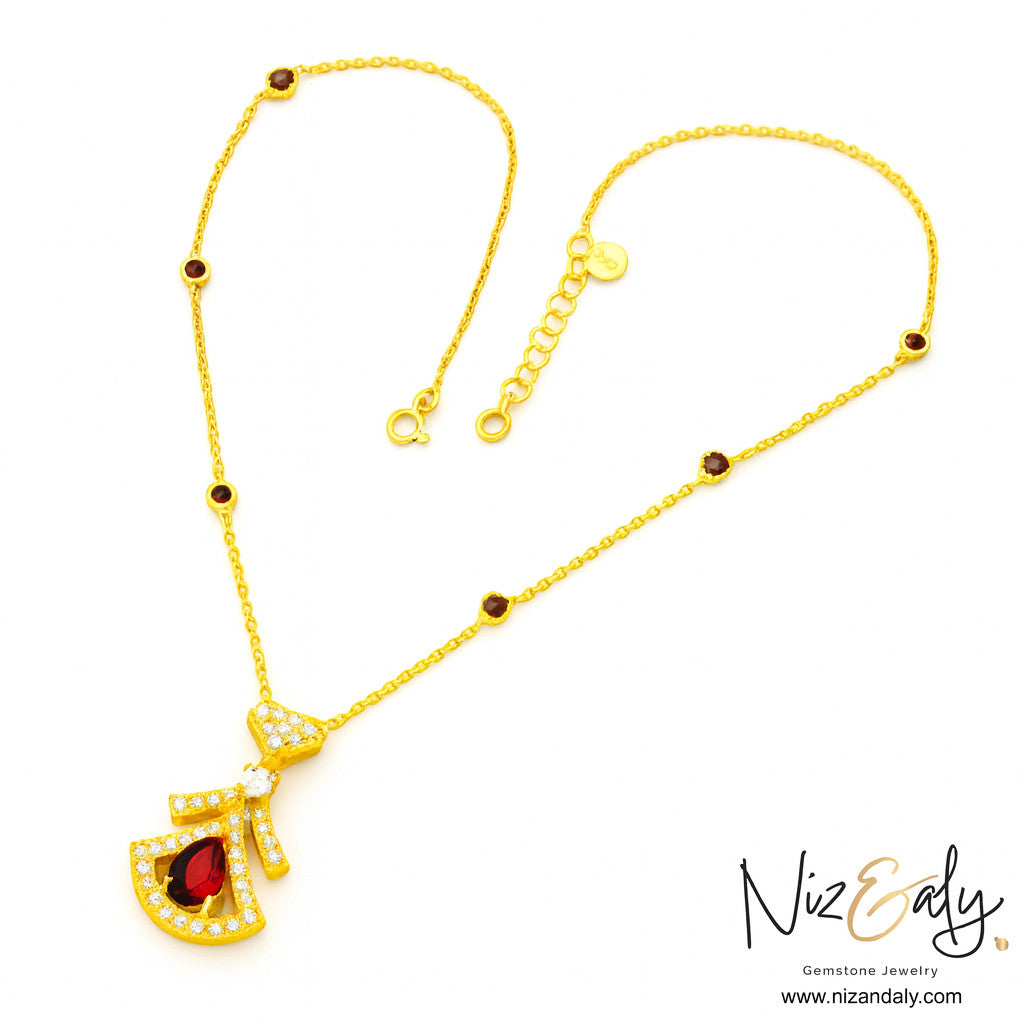 Niz & Aly Midnight Grace gold necklace featuring a deep red garnet fan pendant with clear stone accents and chain gems.