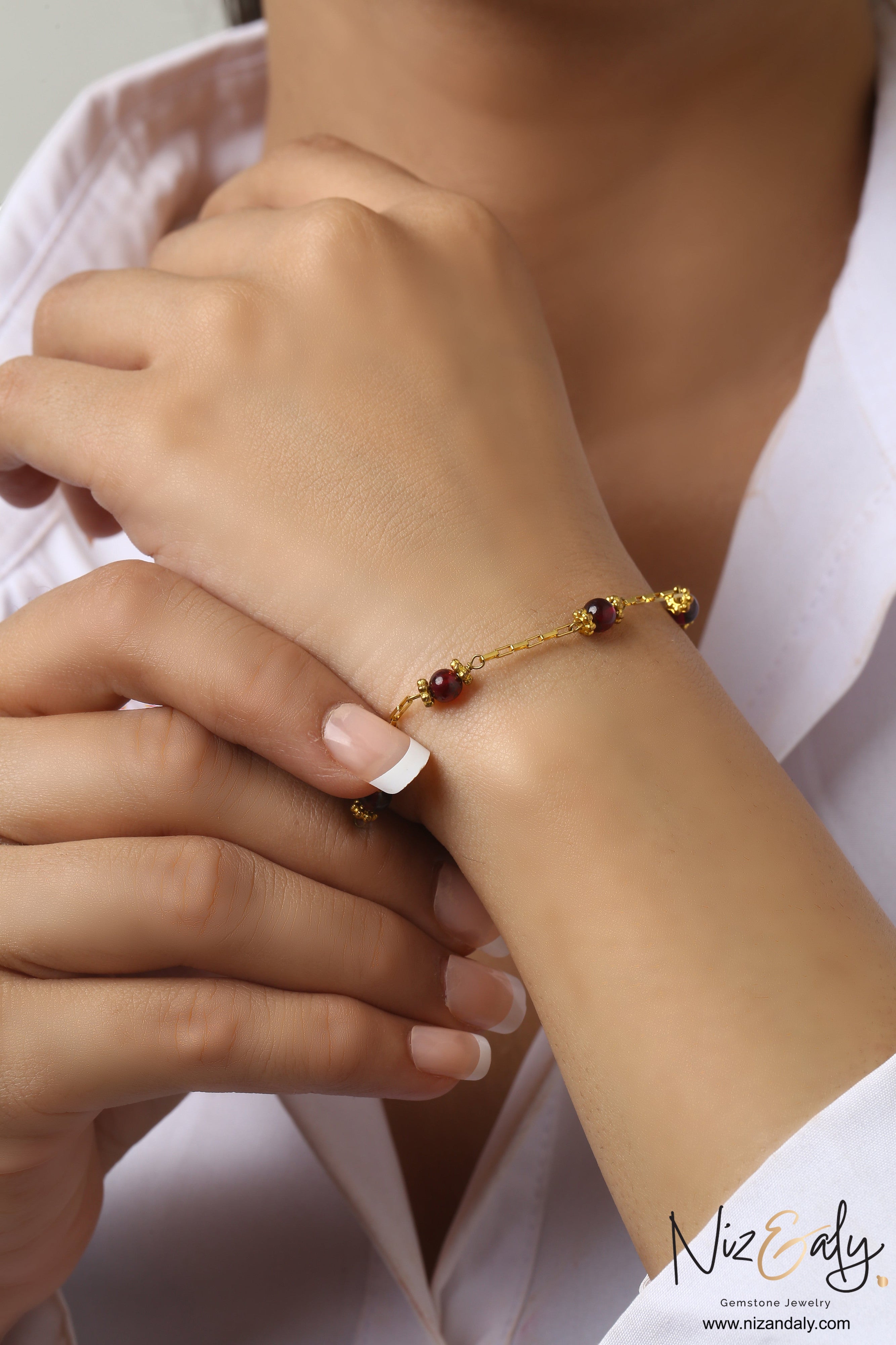 Niz & Aly dainty gold chain bracelet featuring natural burgundy garnet beads worn on a woman's wrist.