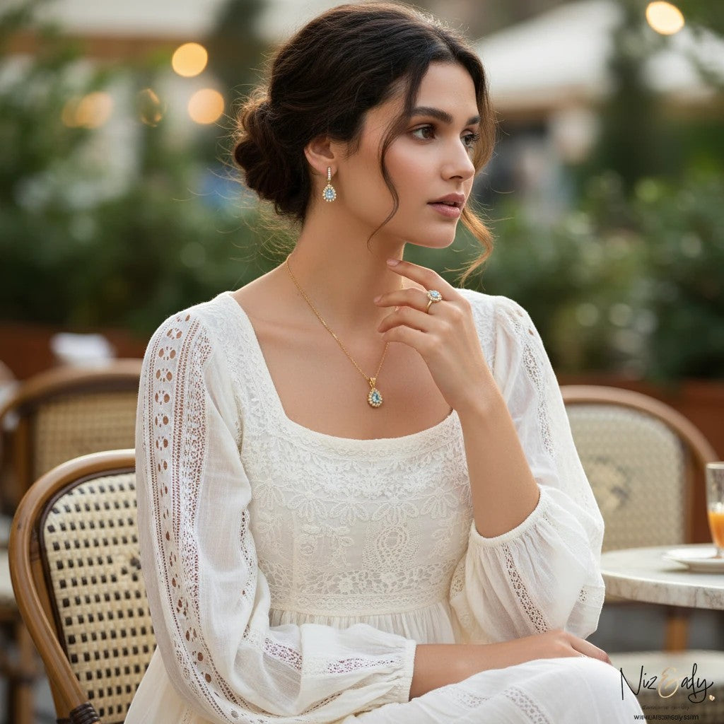 Niz & Aly gold plated jewelry set with pear shaped blue topaz pendant, earrings, and ring worn by a woman in white.