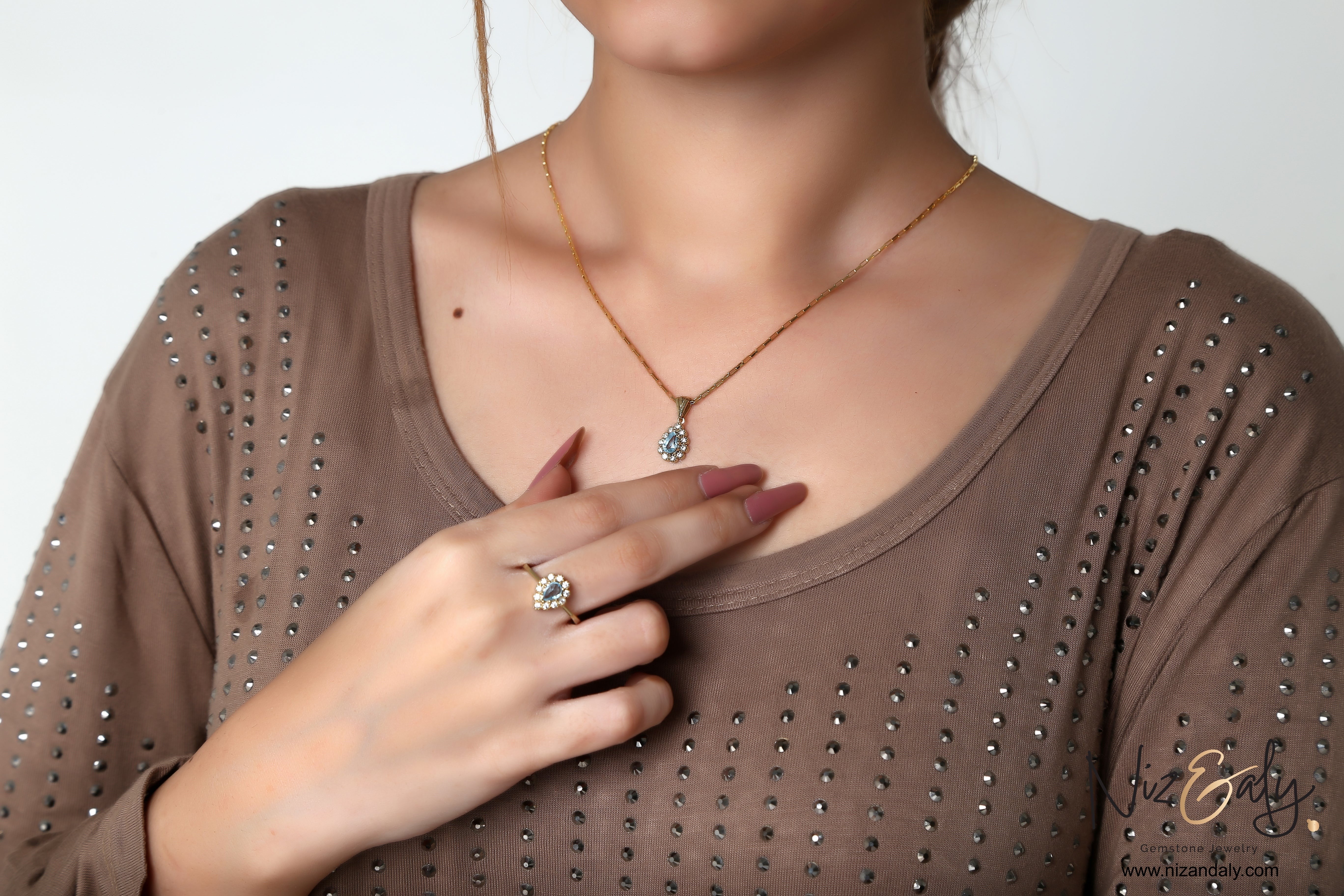 Niz & Aly gold plated jewelry set featuring a pear-shaped natural blue topaz pendant and matching ring on a model