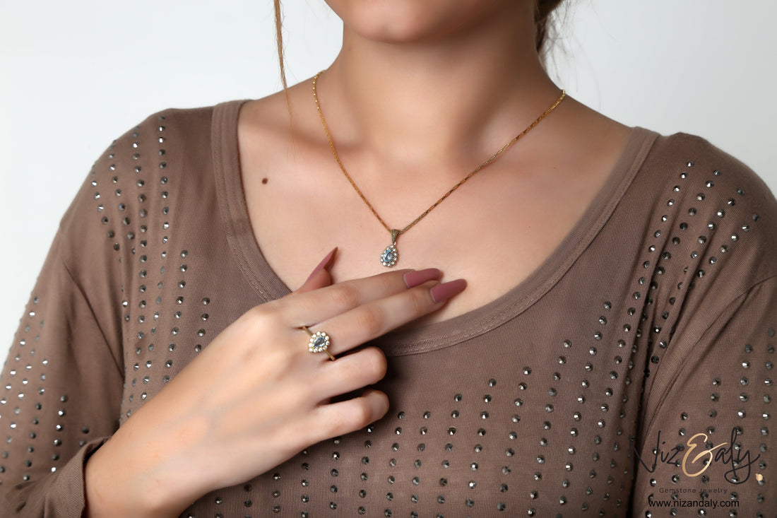 Niz & Aly gold plated jewelry set featuring a pear-shaped natural blue topaz pendant and matching ring on a model