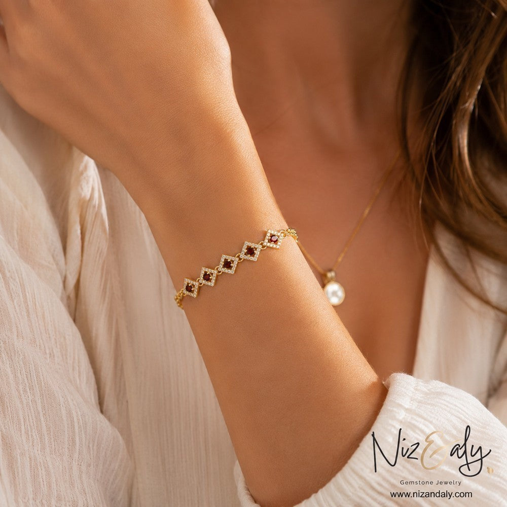 Niz & Aly gold plated silver bracelet featuring diamond-shaped links with red garnet stones and a sparkling halo.