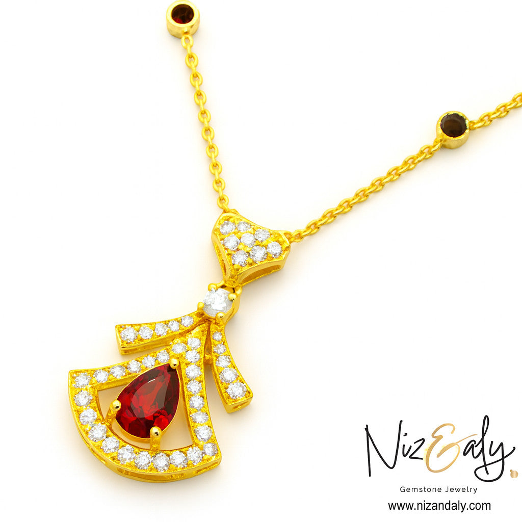 Niz & Aly gold fan-shaped pendant necklace featuring a deep red garnet, clear pavé stones, and dark gemstone accents.