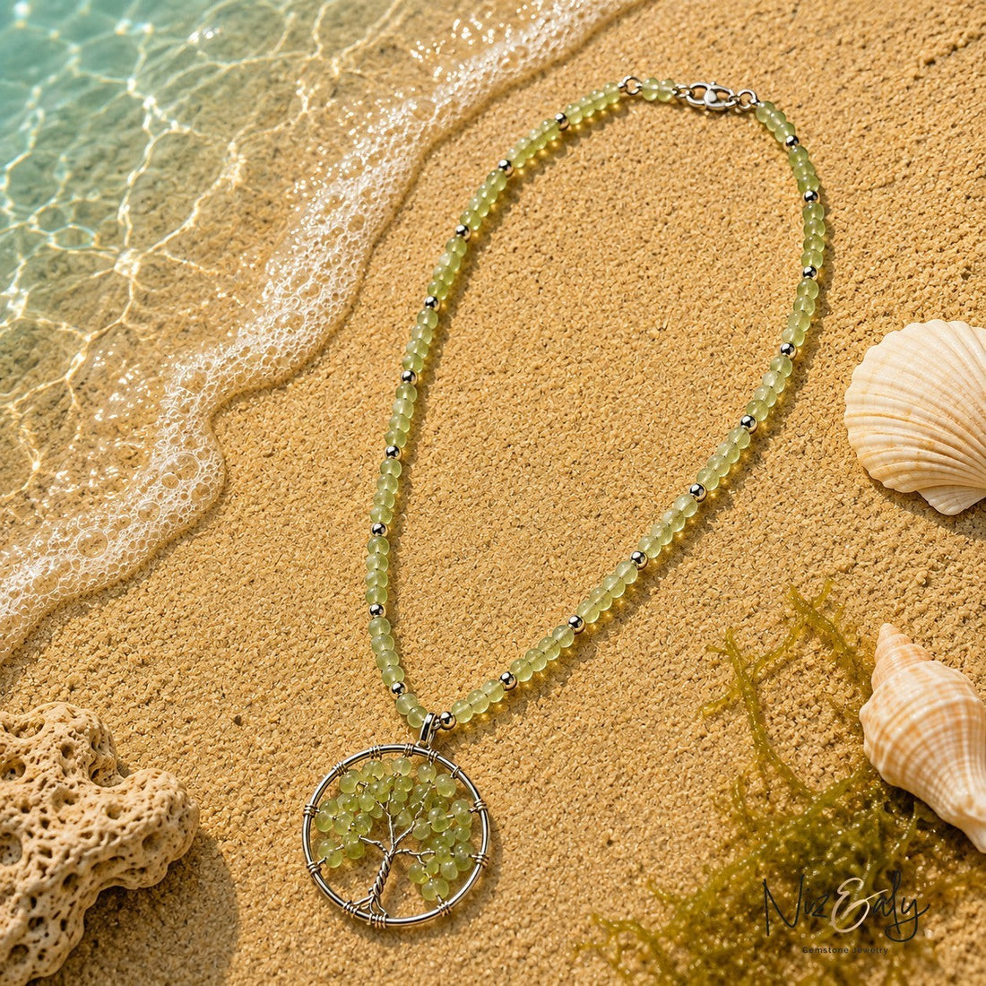 Niz & Aly light green gemstone bead necklace with a tree of life pendant resting on sandy beach shore with seashells.
