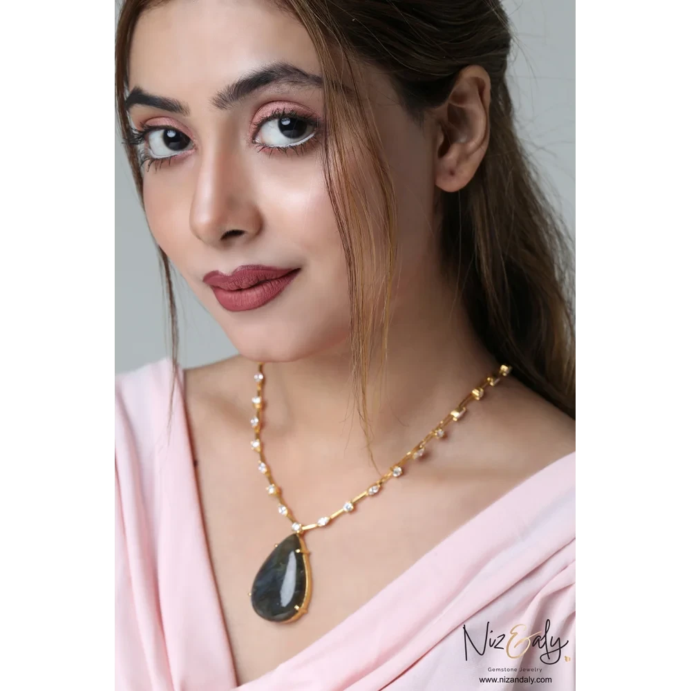 Niz & Aly teardrop labradorite pendant on a gold-toned studded chain worn by a woman in a soft pink top