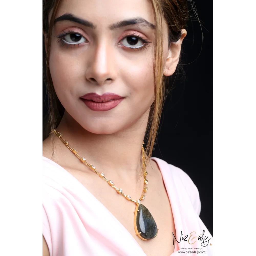 Niz & Aly Midnight Oracle labradorite teardrop pendant on a gold-toned studded chain worn by a woman.