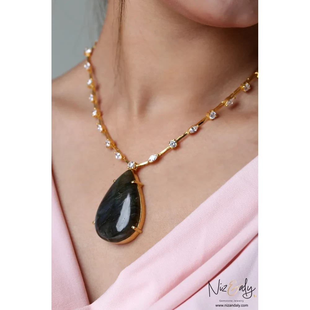 Niz & Aly teardrop labradorite pendant on a gold-toned studded chain worn by a woman in a soft pink top.