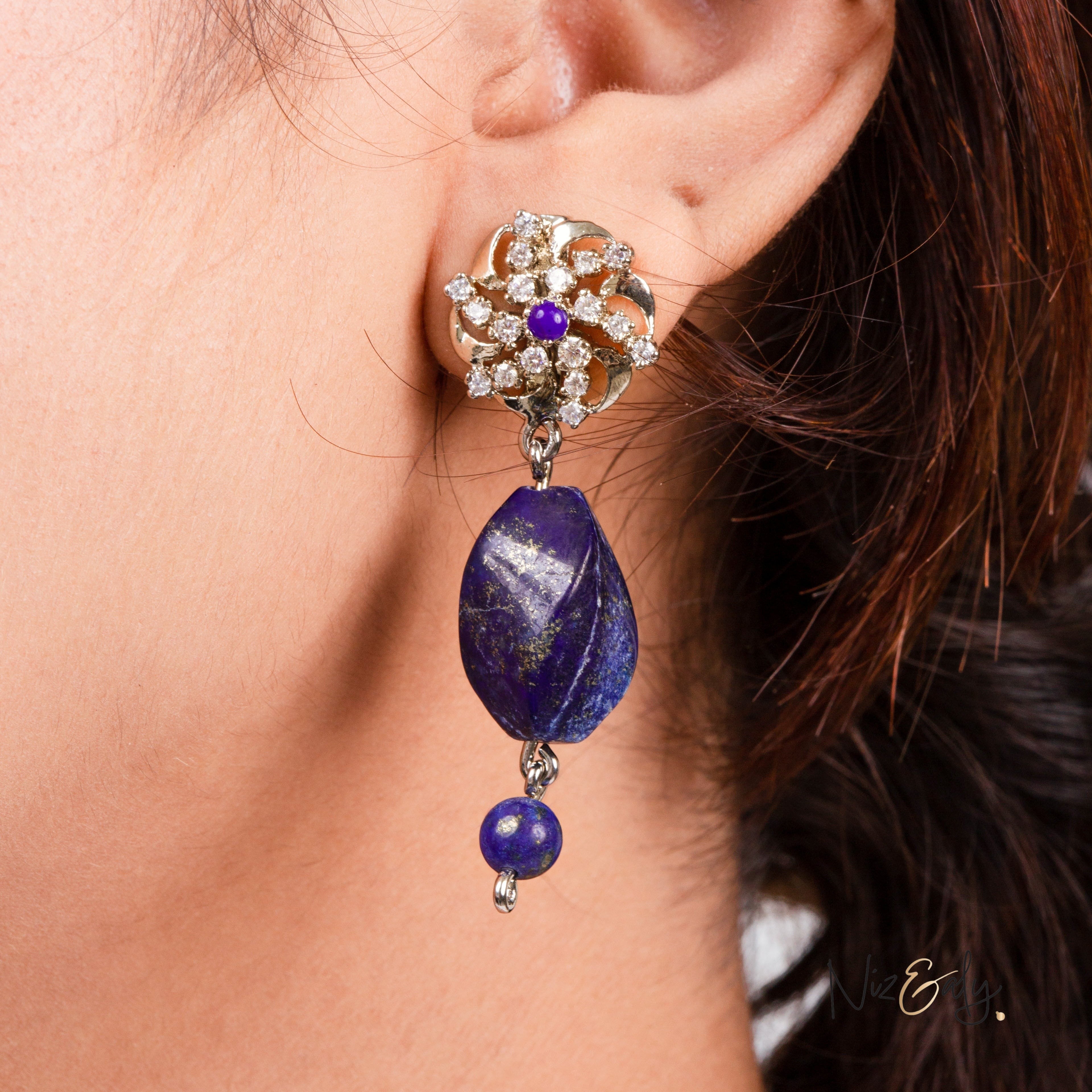 Niz & Aly lapis lazuli drop earring featuring a floral diamond stud and a faceted deep blue stone on a silver setting