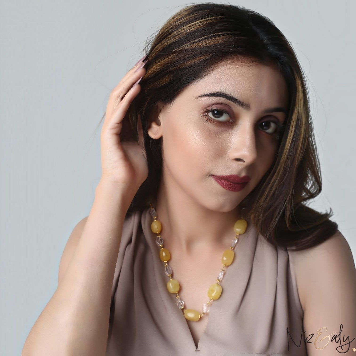 A woman wearing a Niz & Aly handcrafted necklace featuring pastel lemon chiffon jade and clear icy quartz beads.