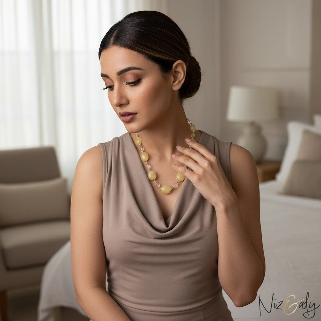 A woman wearing a Niz & Aly handcrafted necklace of lemon chiffon jade and icy quartz beads with a beige cowl neck top.