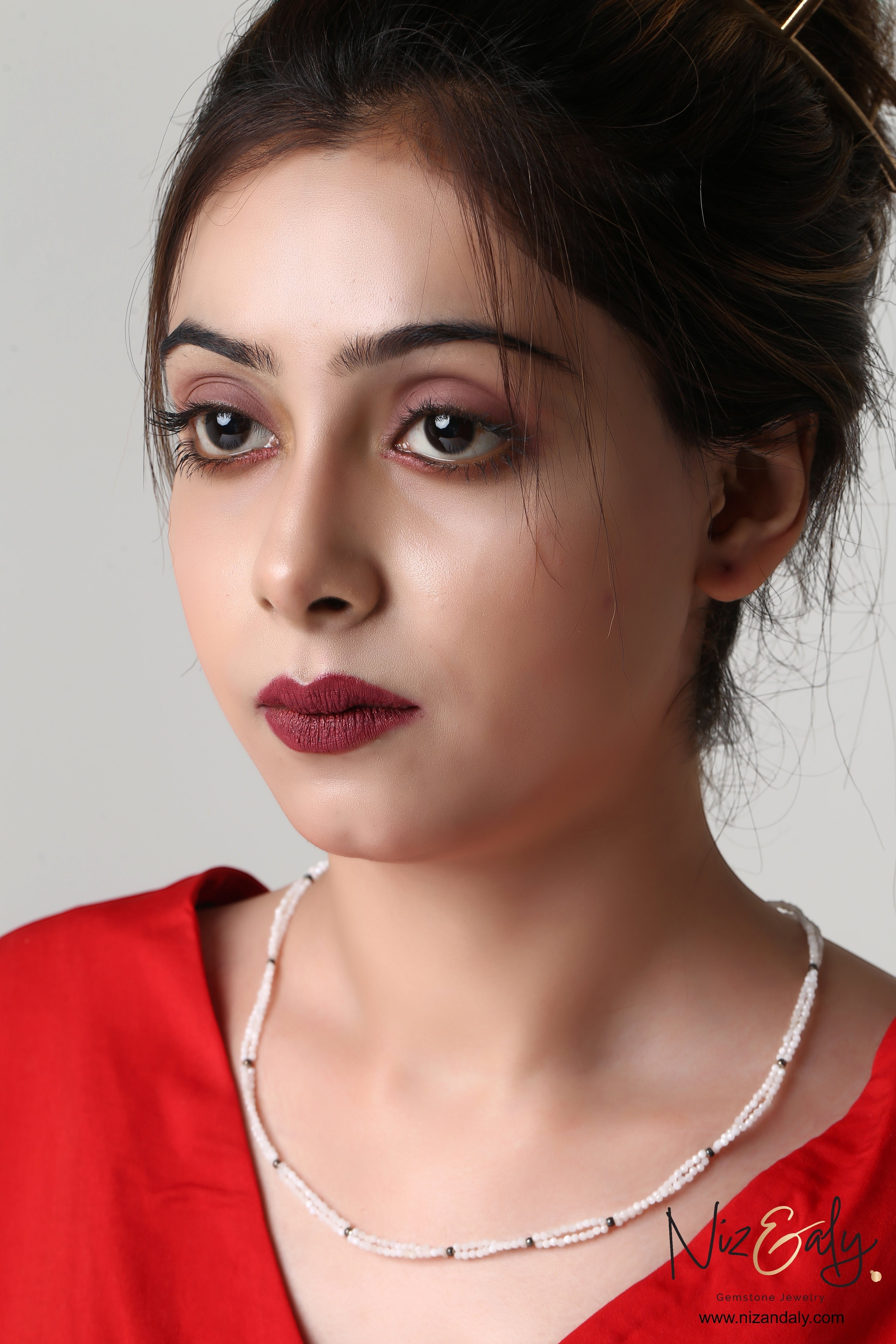 Niz & Aly dainty double-strand milky quartz necklace worn by a woman in a red top, featuring delicate white beads.